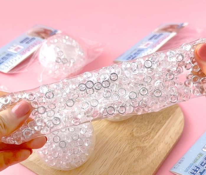 Clear gel with embedded beads held by a hand on a pink background