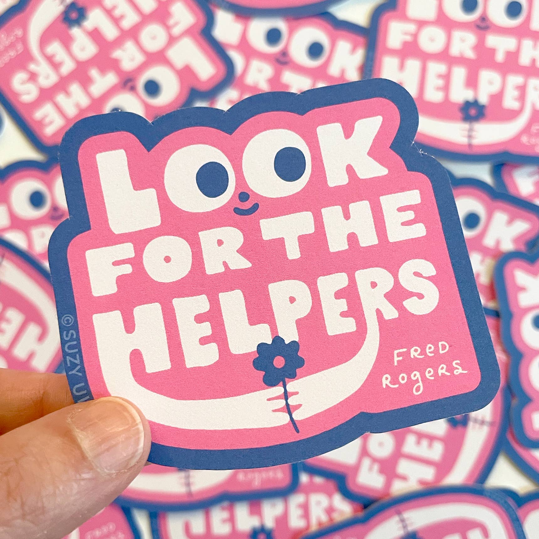Sticker with 'Look for the Helpers' text held by a hand, with more stickers in the background.