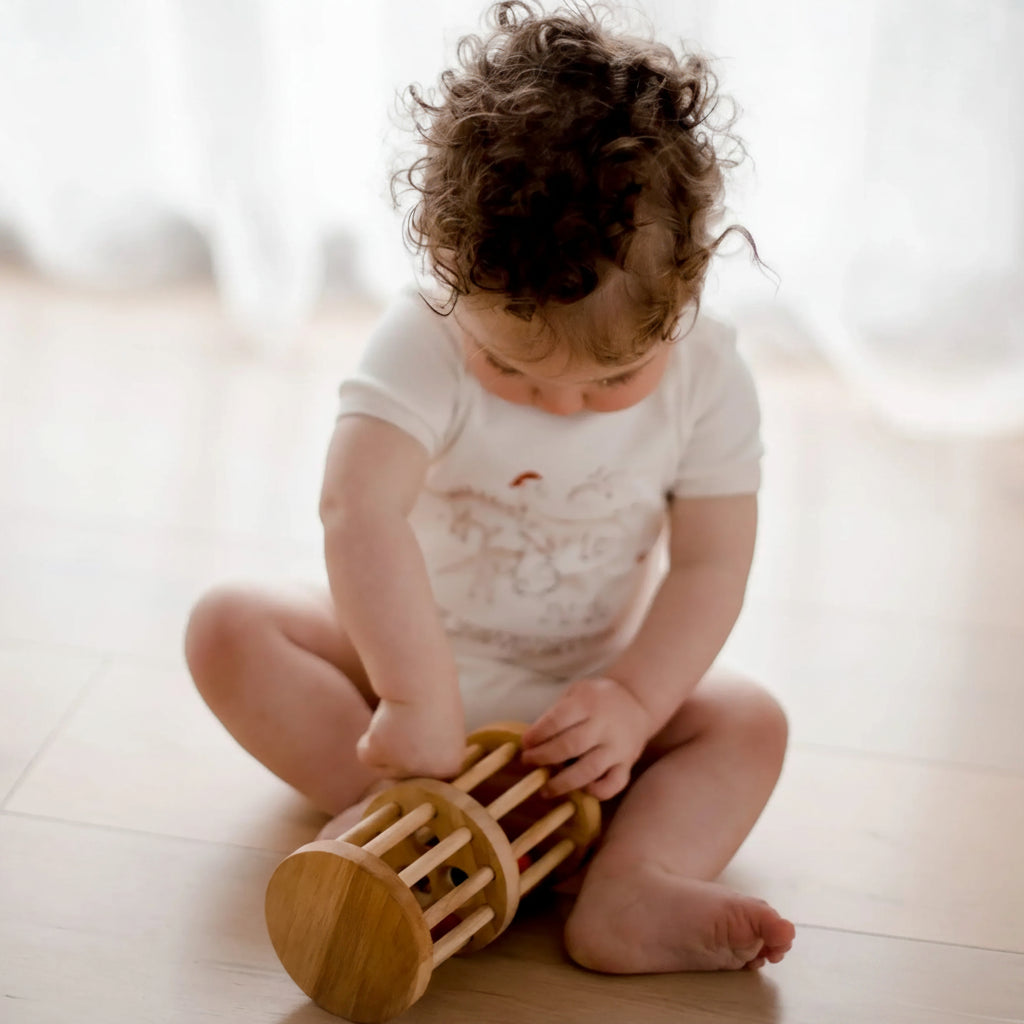 Child playing with a wooden toy on a light wooden floor.