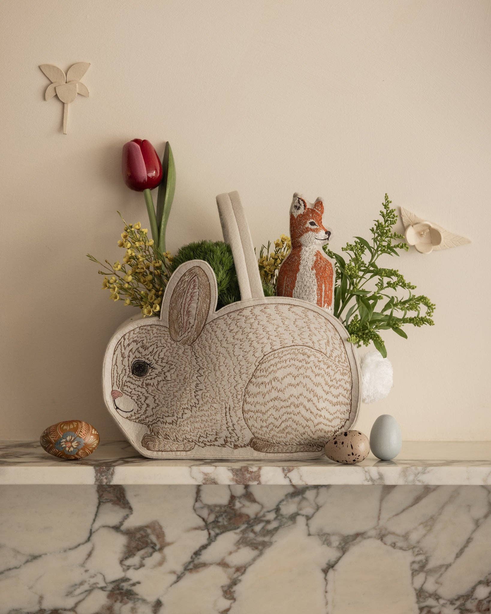 Decorative rabbit-shaped basket with a fox figurine and flowers on a marble surface.