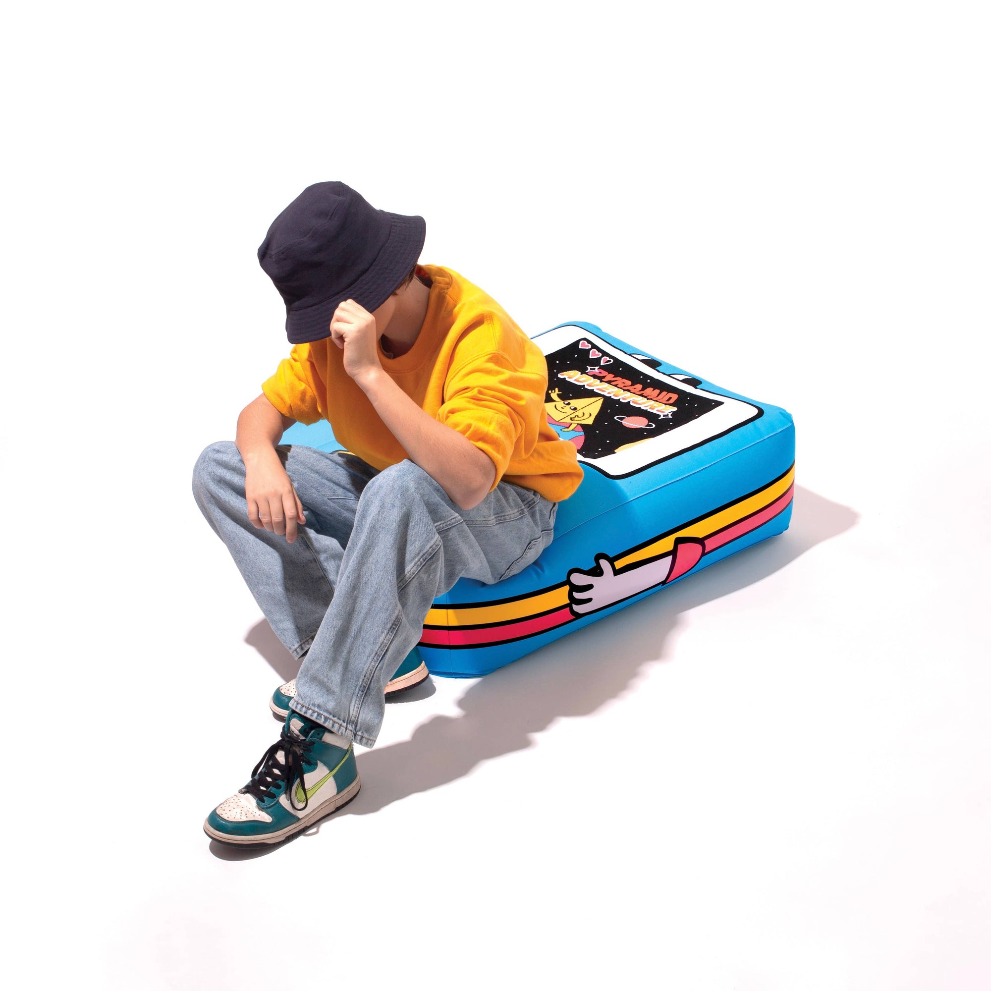 Person sitting on a colorful, retro-style suitcase with a white background