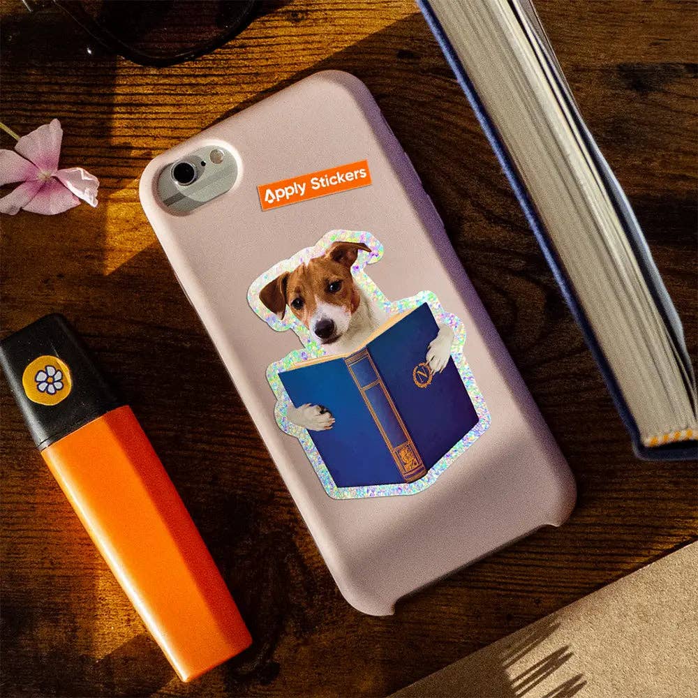 Phone case with a dog sticker on a wooden surface with a book and orange lighter.