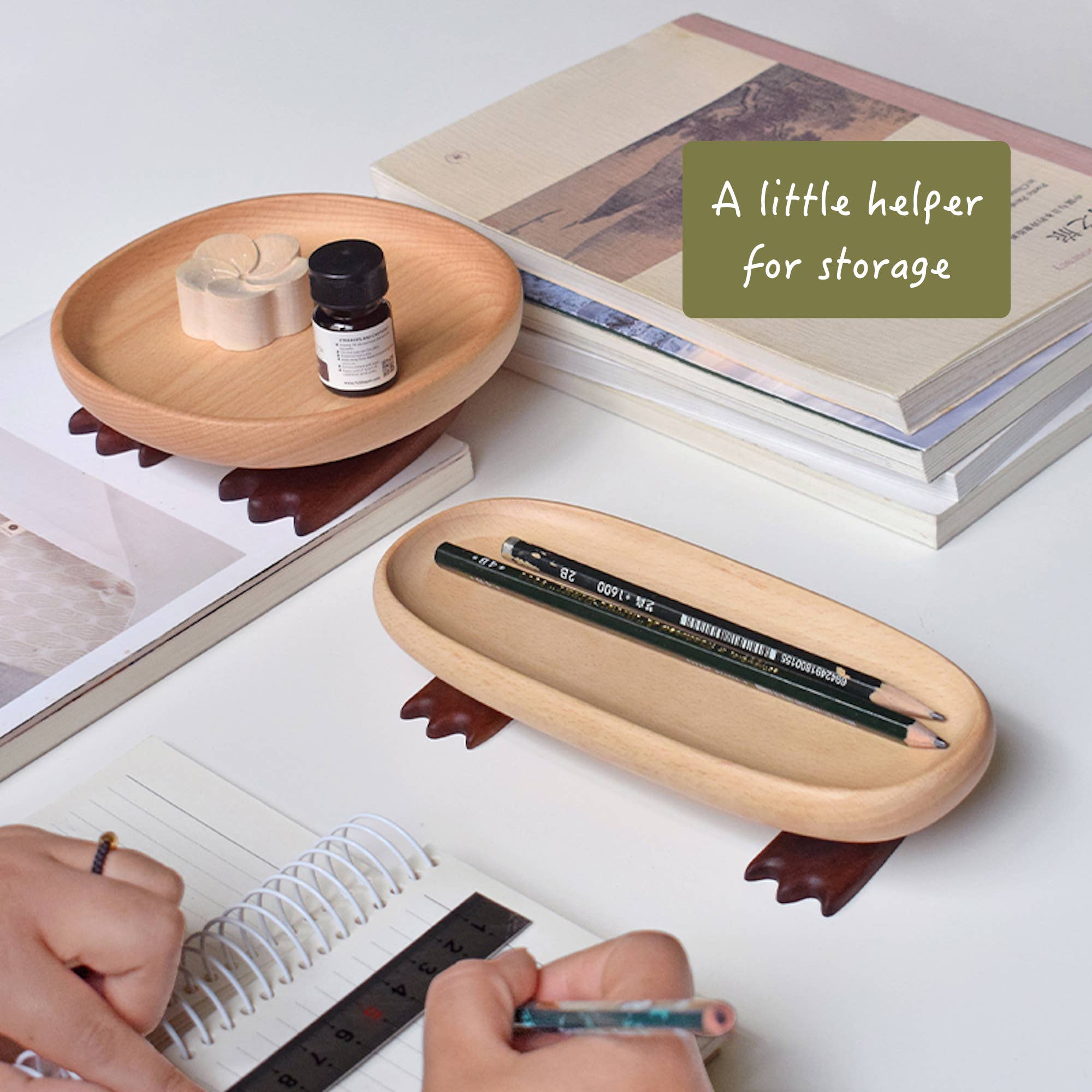 Wooden tray holding a pencil and small bottle, on a surface with books and stationery items.