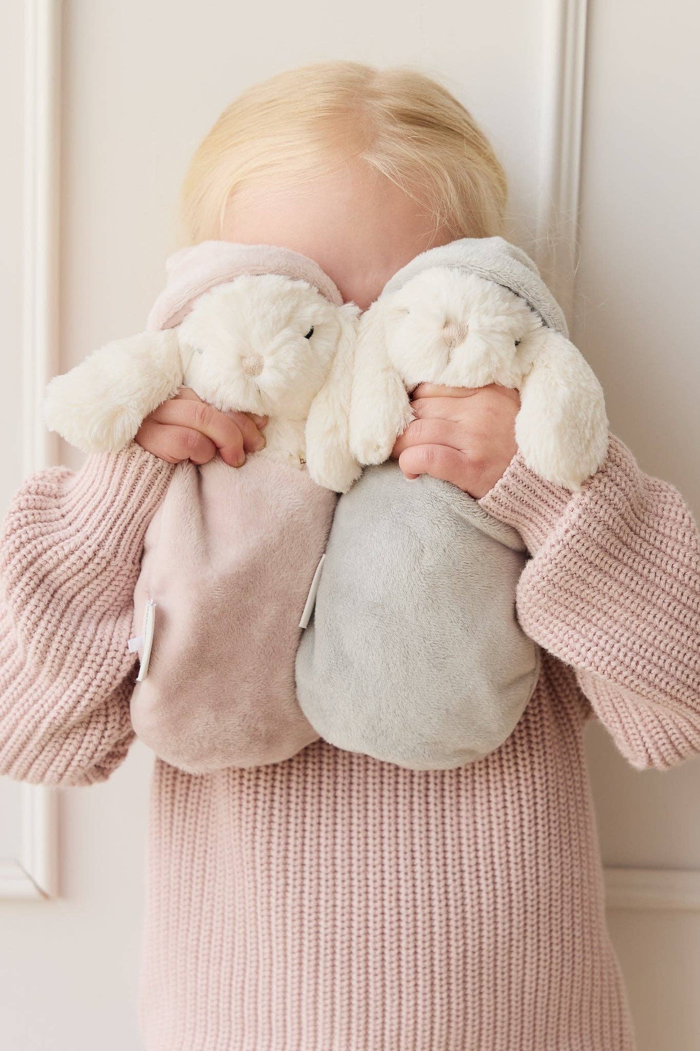 Child holding two plush toys against a white background