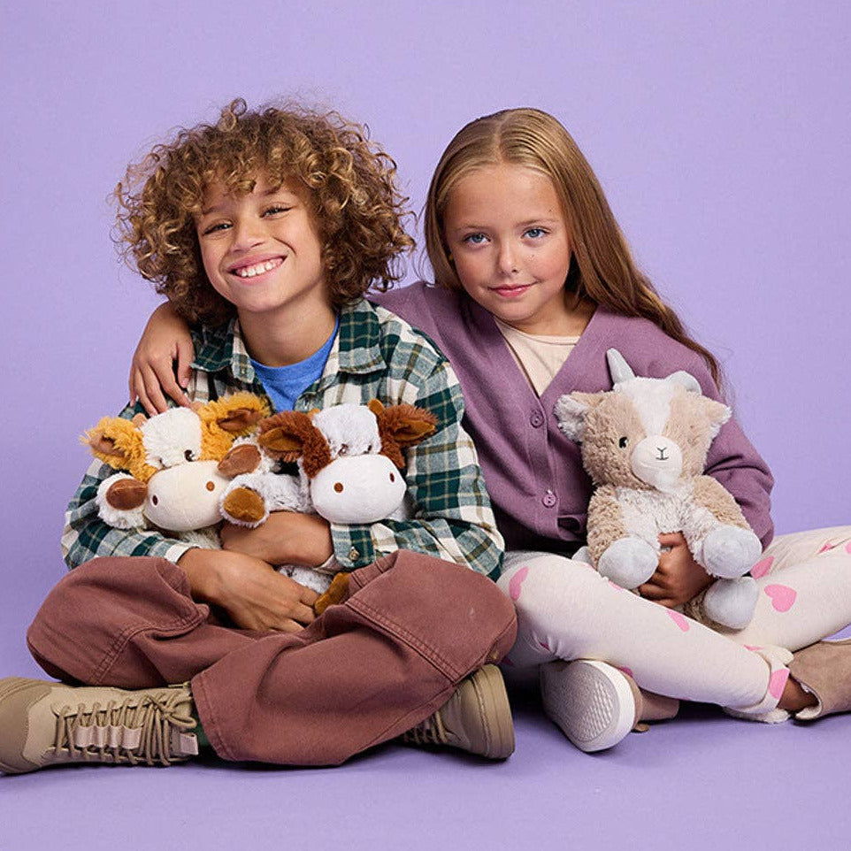 Two children sitting together holding stuffed animals against a purple background