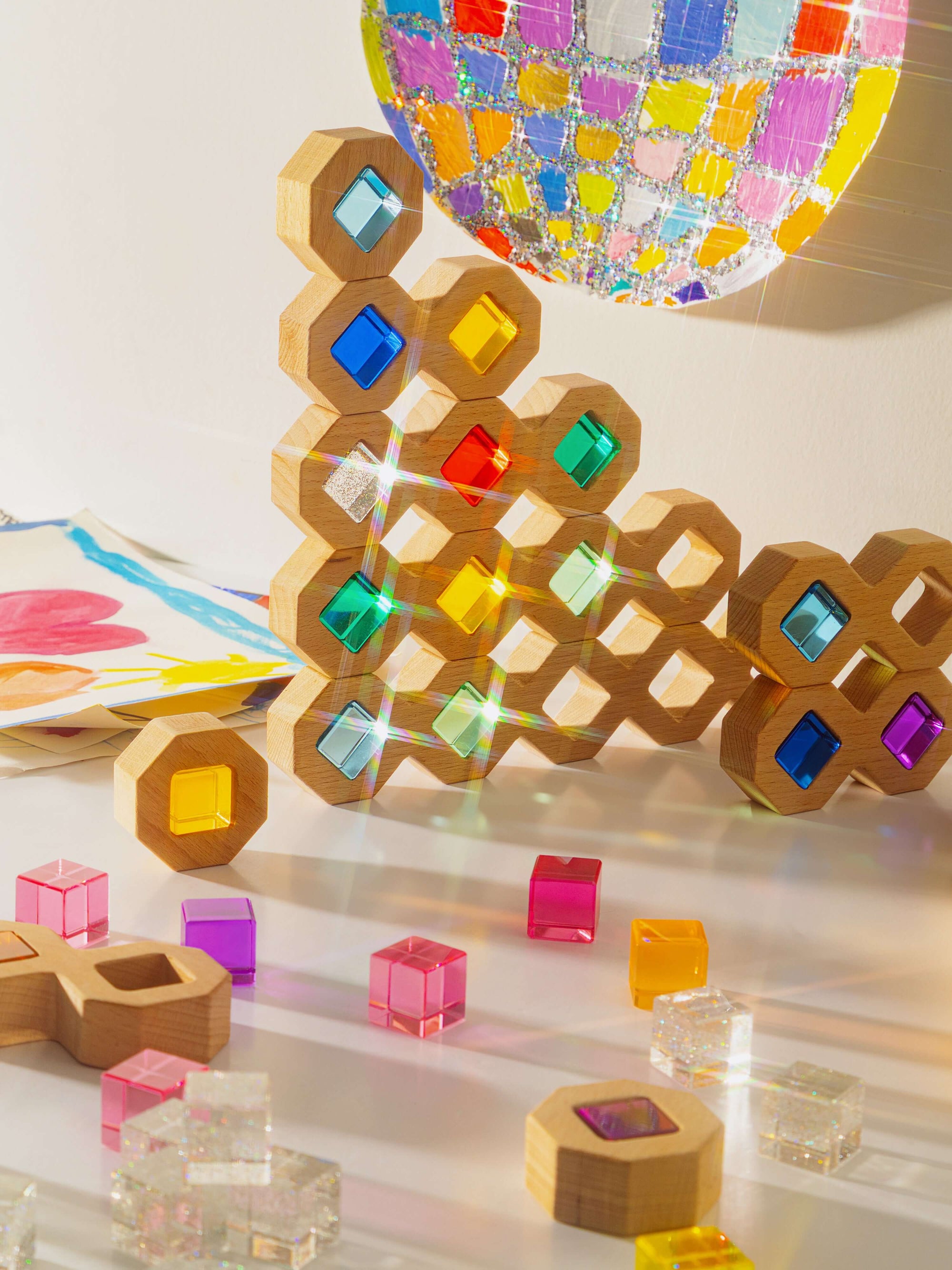 Colorful geometric wooden blocks on a reflective surface with a mosaic wall in the background