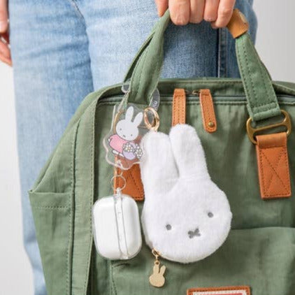 Green bag with plush bunny keychains attached, held by a person wearing blue jeans.