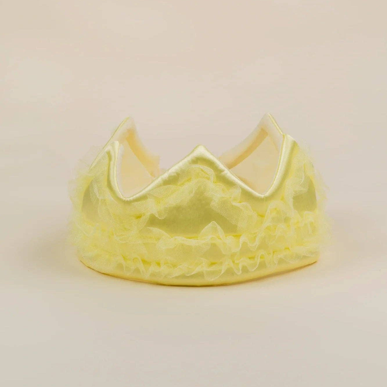 A light yellow ruffled tiara crown with a satin trim, photographed on a plain beige background.