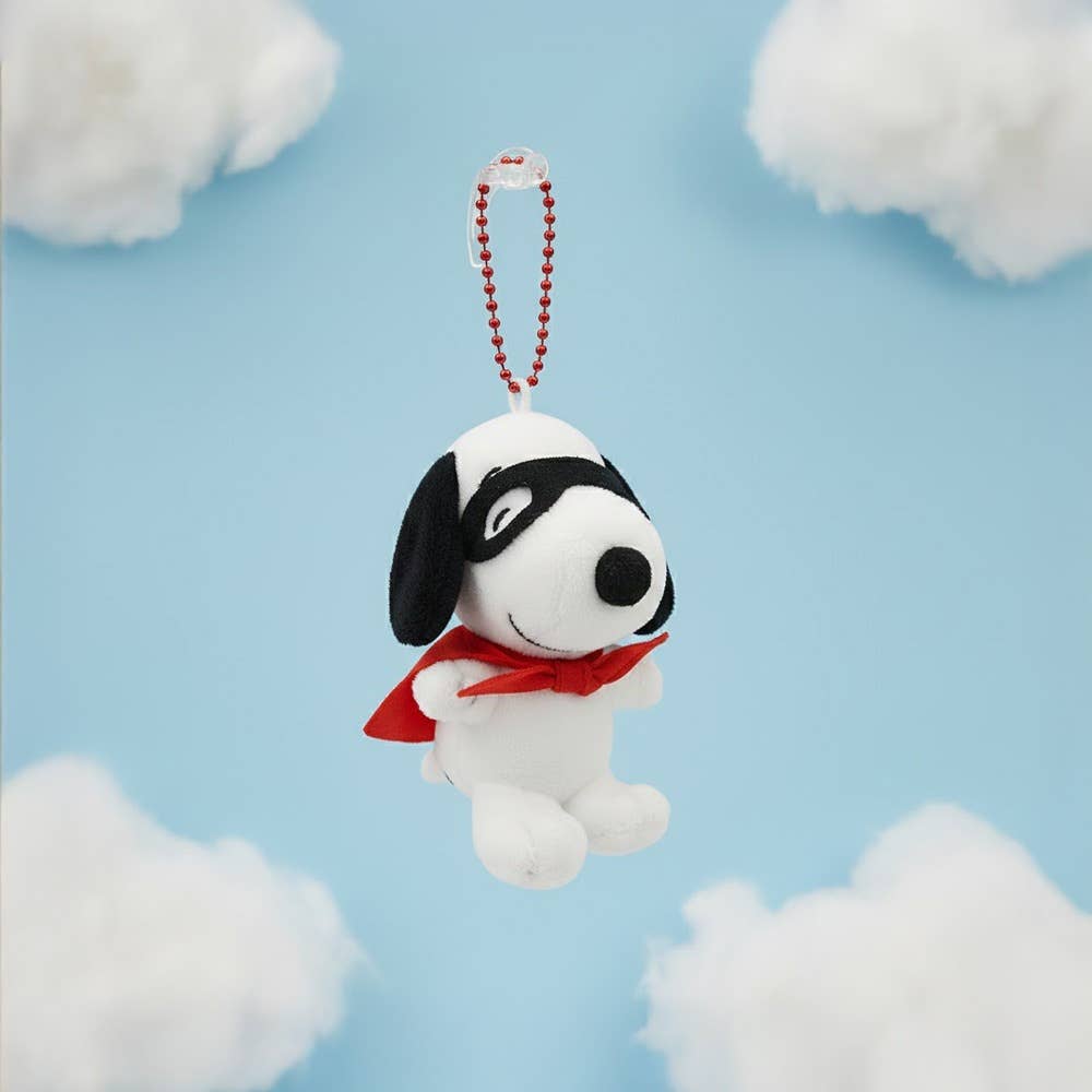 Dog-shaped keychain with a red cape against a blue background with white clouds