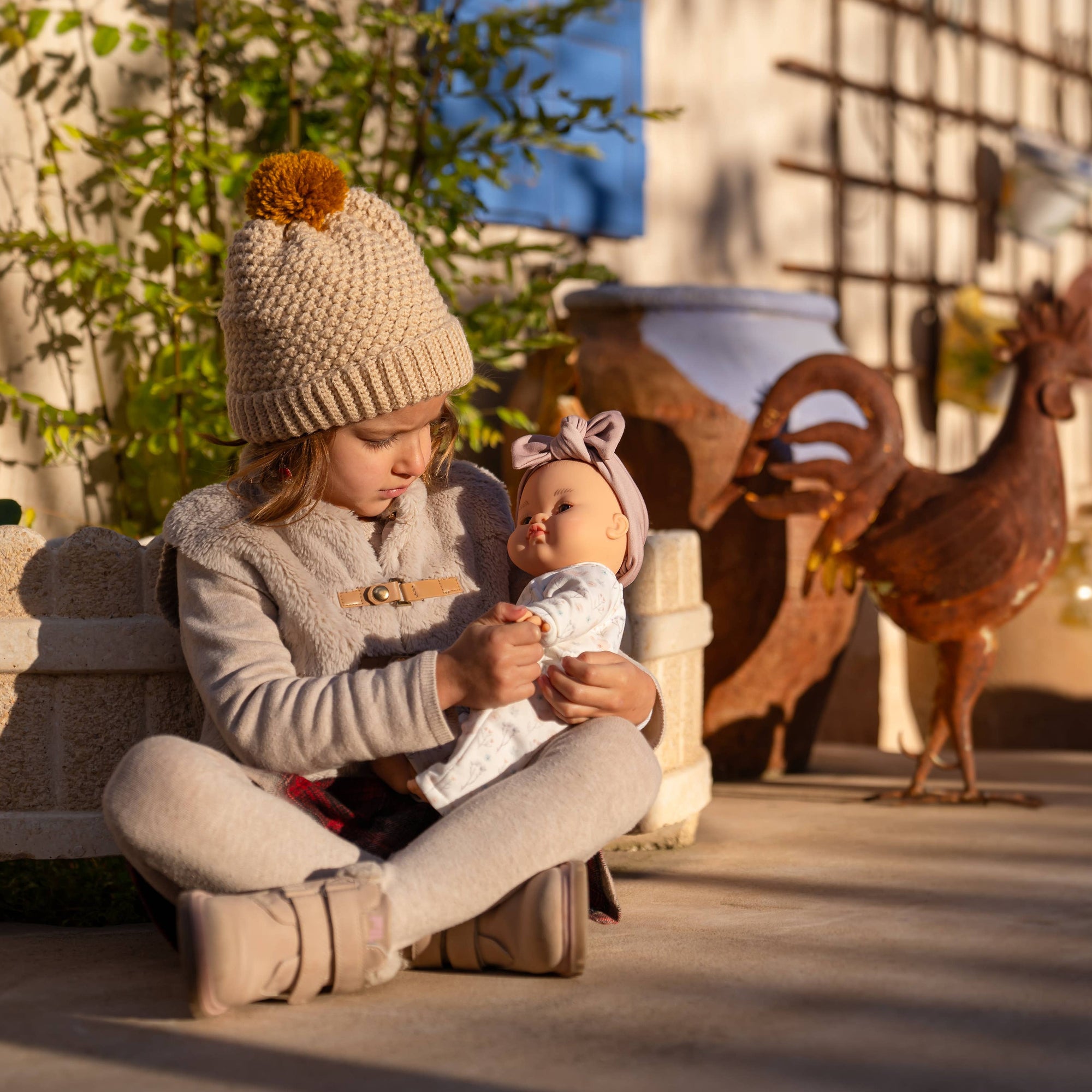 Two children playing with a baby in an outdoor setting with toys and plants.