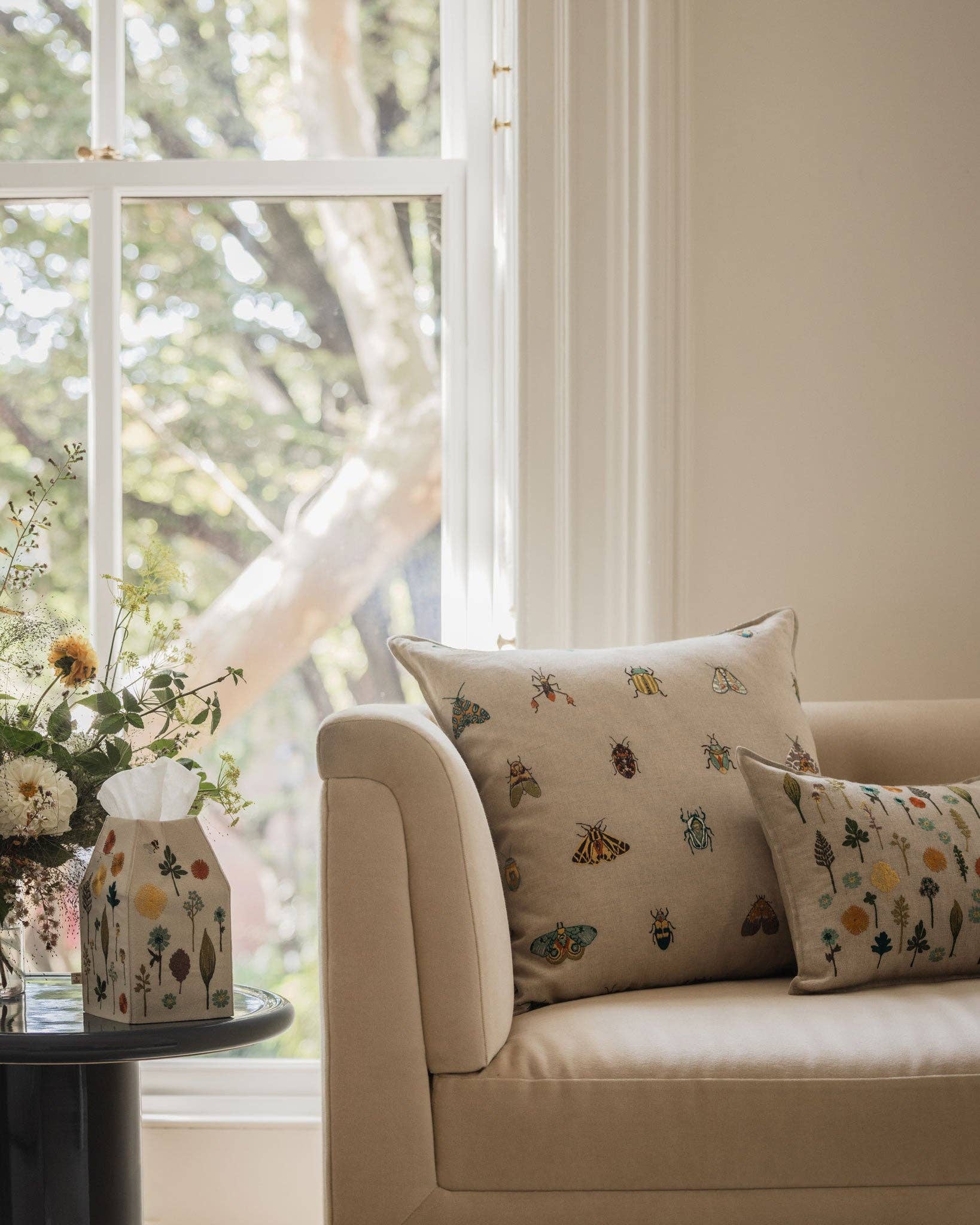 Beige sofa with patterned cushions in a room with large windows and a decorative vase.