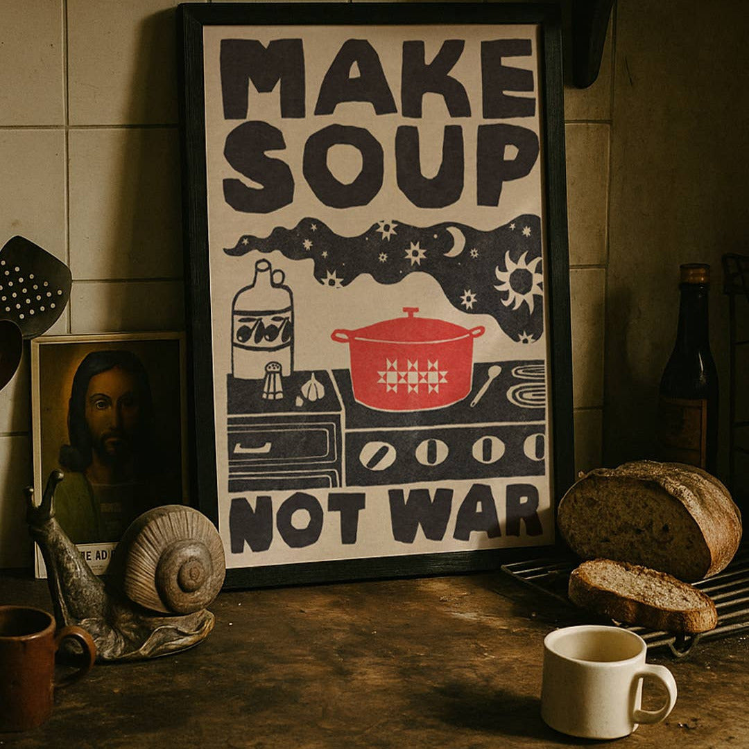 Framed poster with 'Make Soup Not War' design on a kitchen counter with bread and a mug.