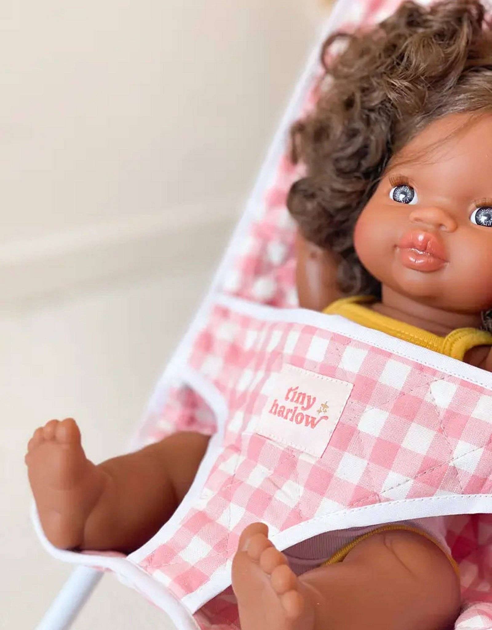 Doll wearing a pink checkered outfit with 'tiny harlow' branding.