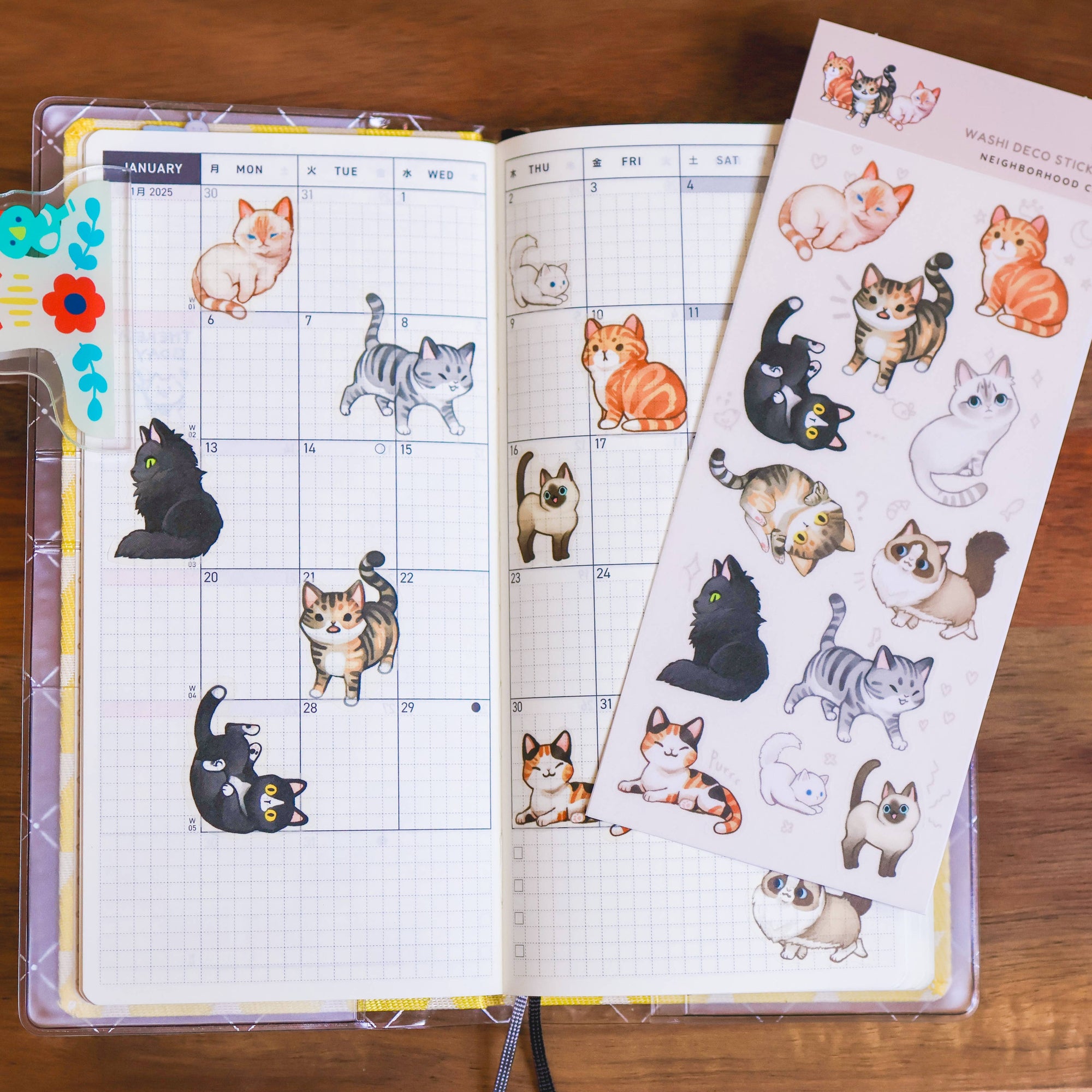 Calendar with cat illustrations and a sheet of additional cat stickers on a wooden surface.