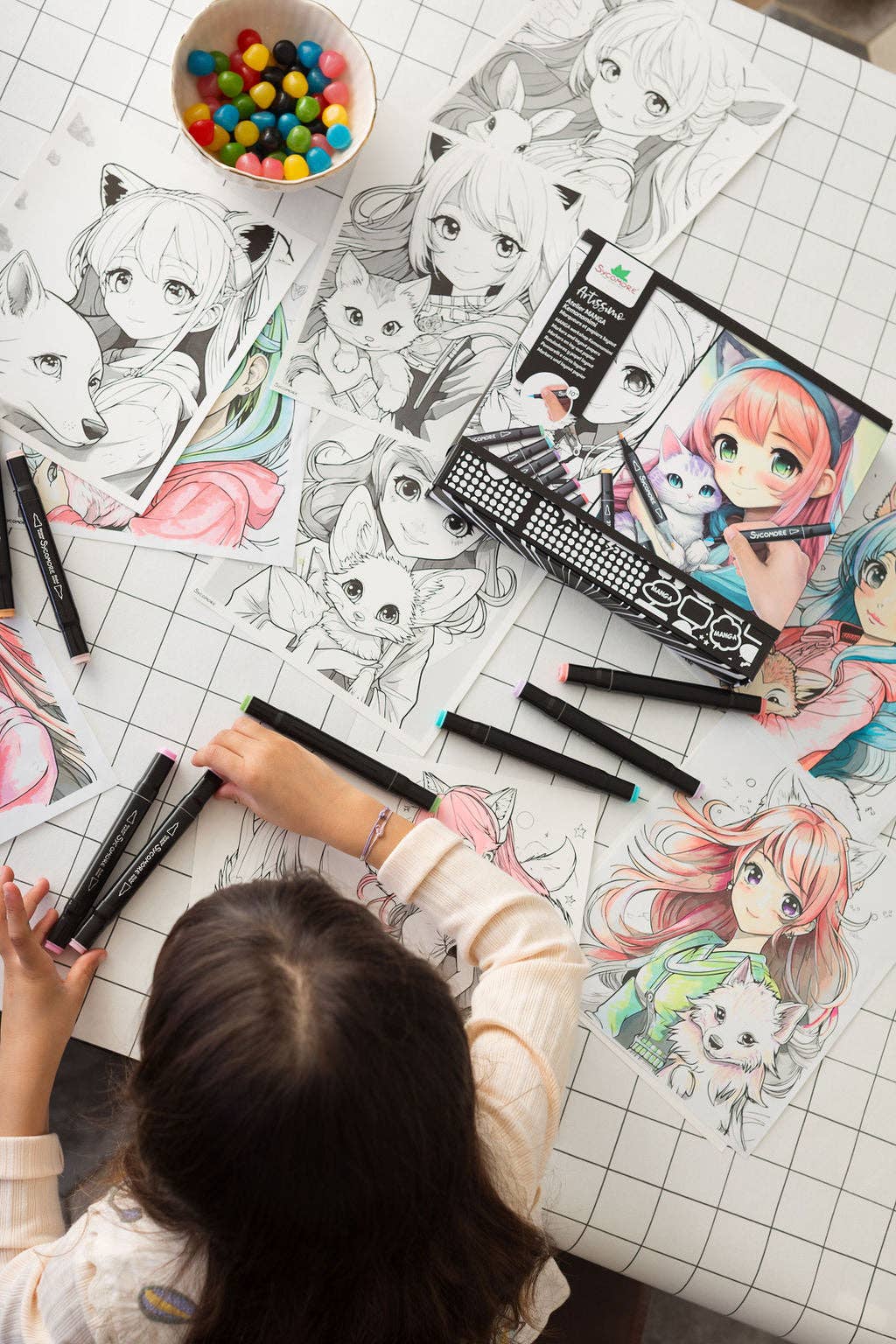 Child coloring anime characters with markers on a grid-patterned table.