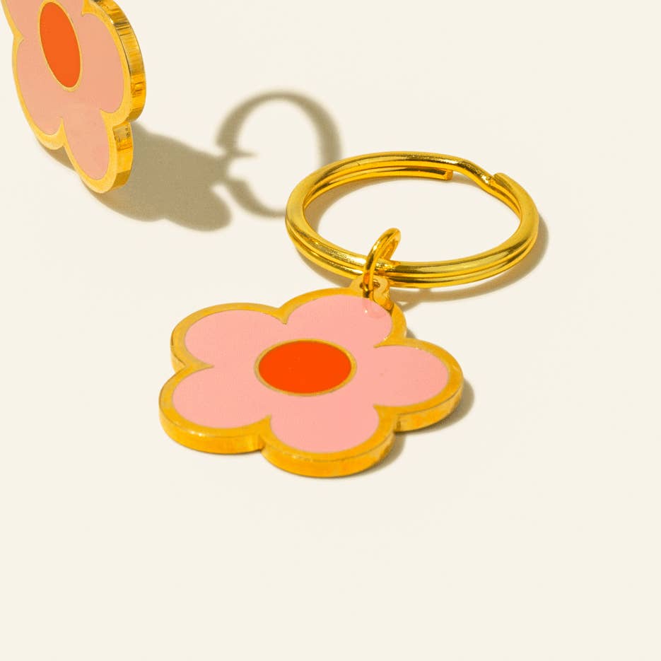 Flower-shaped keychain with pink petals and orange center on a beige background