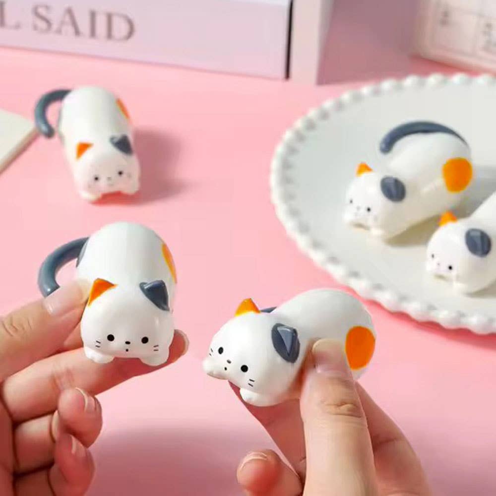 Small cat-shaped figurines held by a hand on a pink background