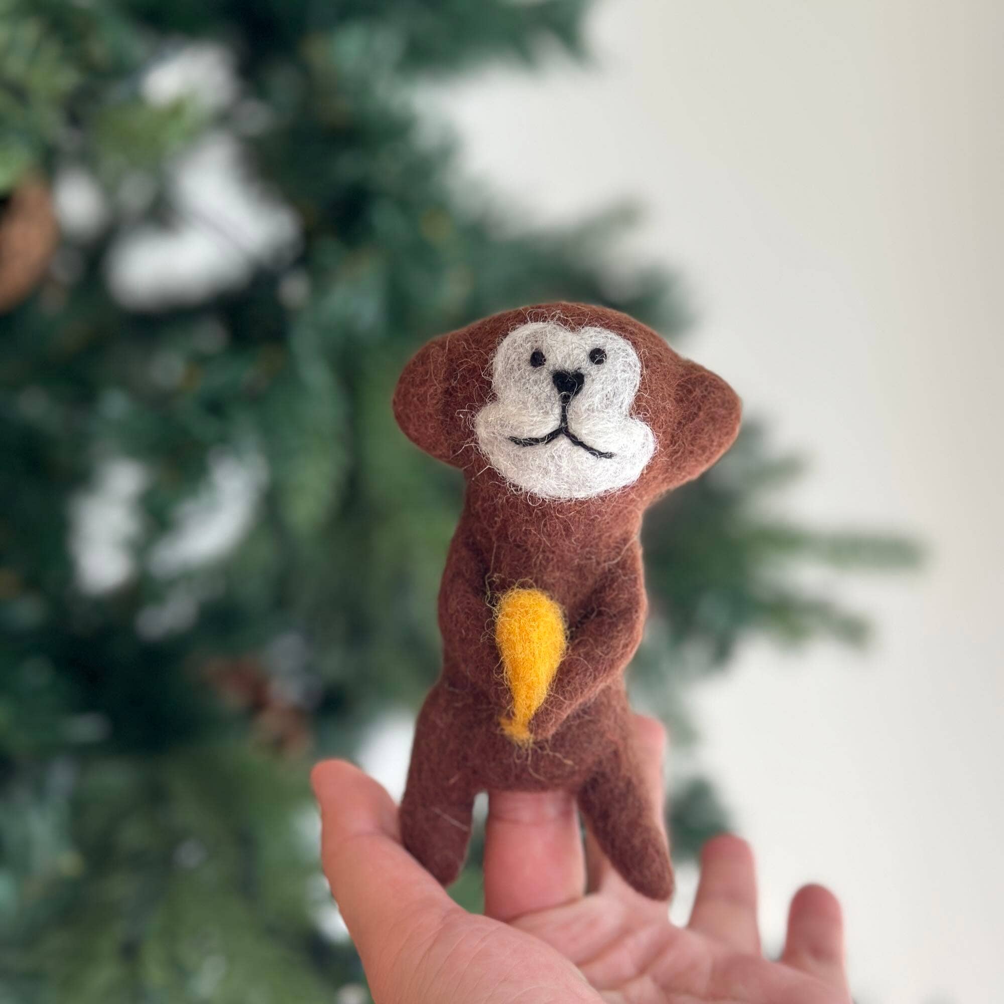Hand holding a small monkey figurine with a blurred Christmas tree background