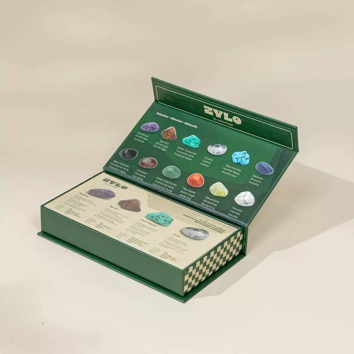Open green box with ZYLO brand name containing various stones on a beige background