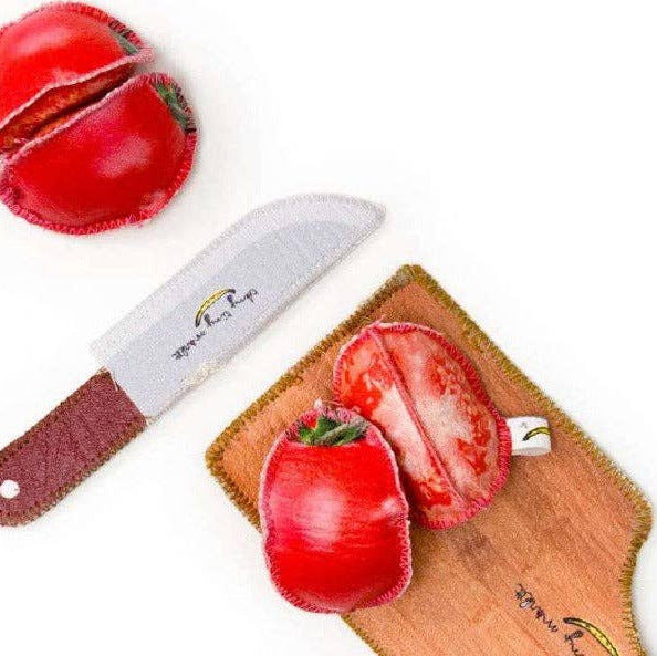A toy tomato cut in half, a wooden cutting board, and a toy chef's knife.