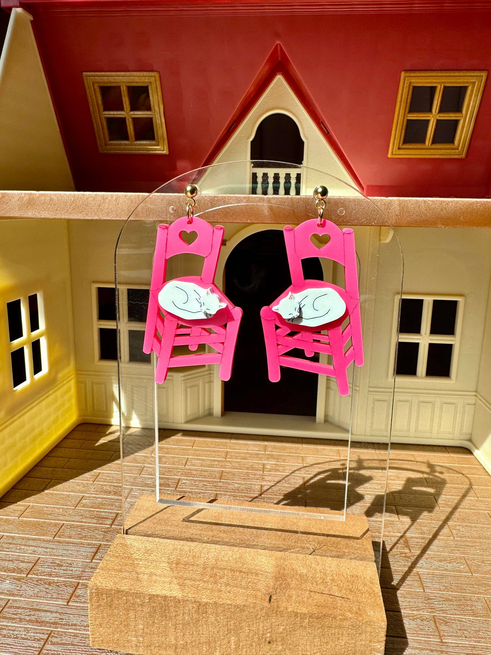 Pink chair-shaped earrings on a clear stand with a miniature house in the background