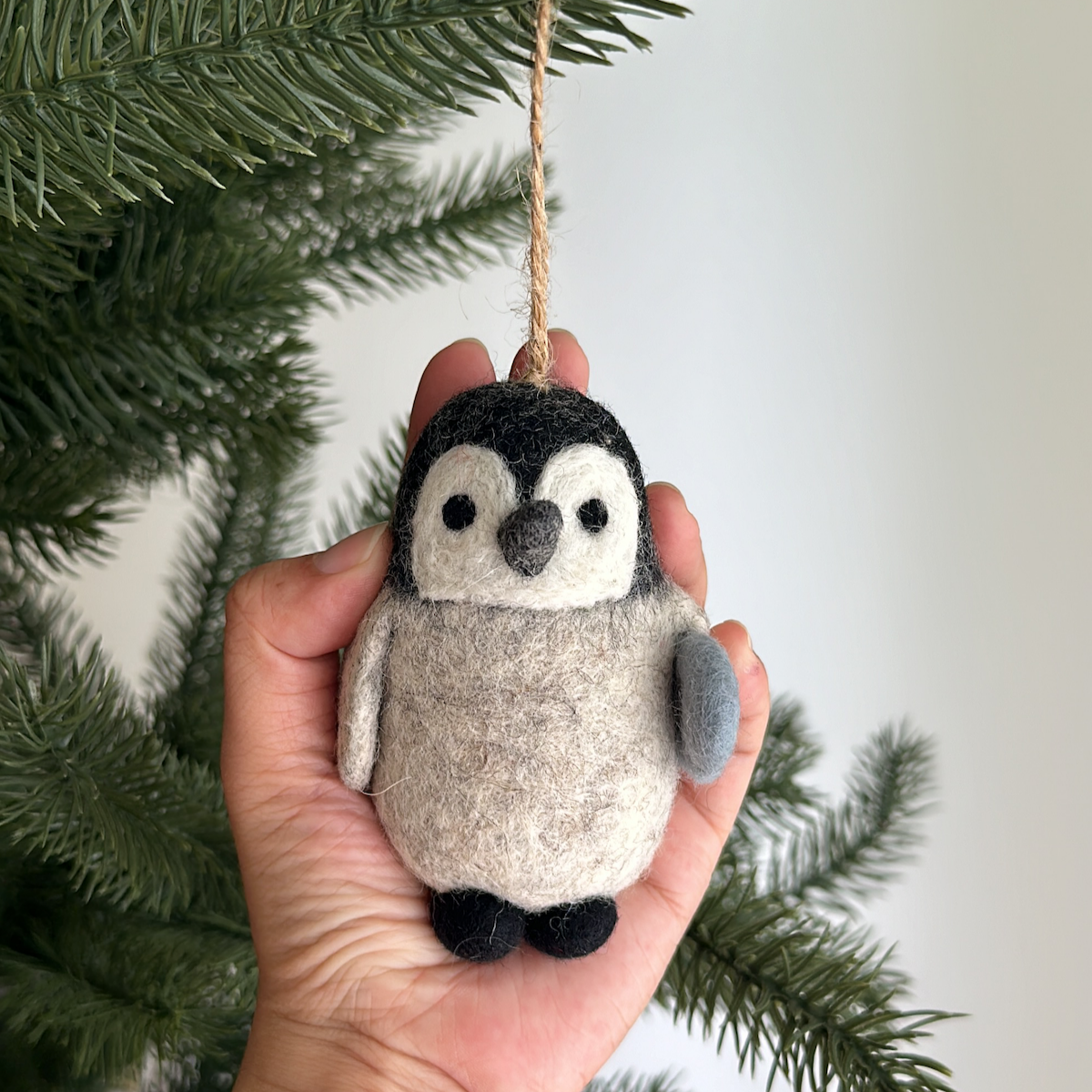Hand holding a felt penguin ornament against a Christmas tree background