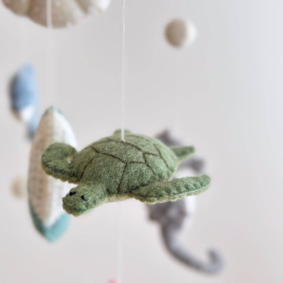 Green turtle-shaped felt mobile piece  on a white background