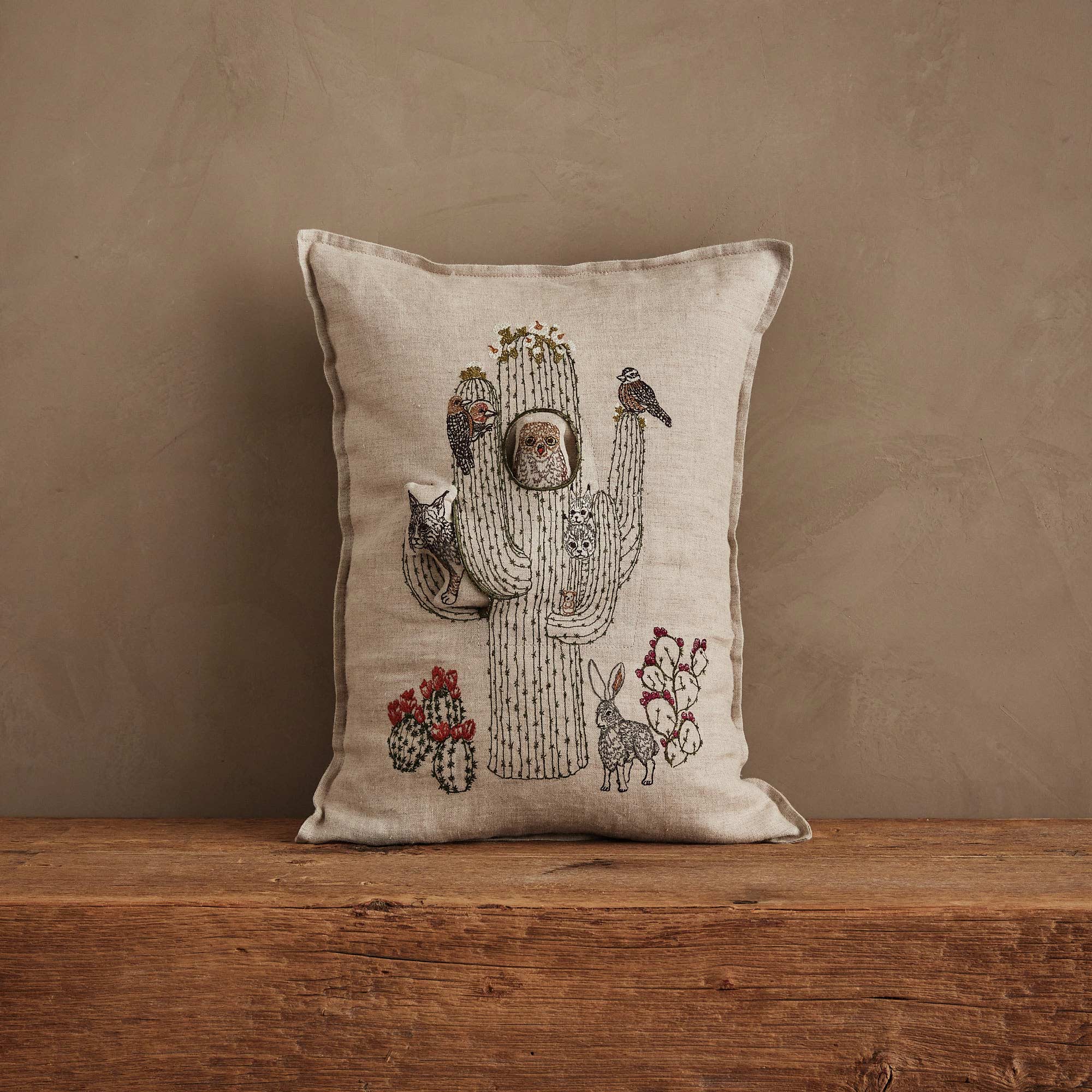 Decorative pillow with a cactus and animal design on a wooden surface and brown background
