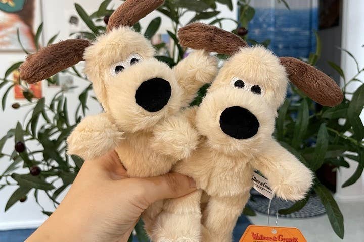Two plush dog toys held by a hand with a plant in the background