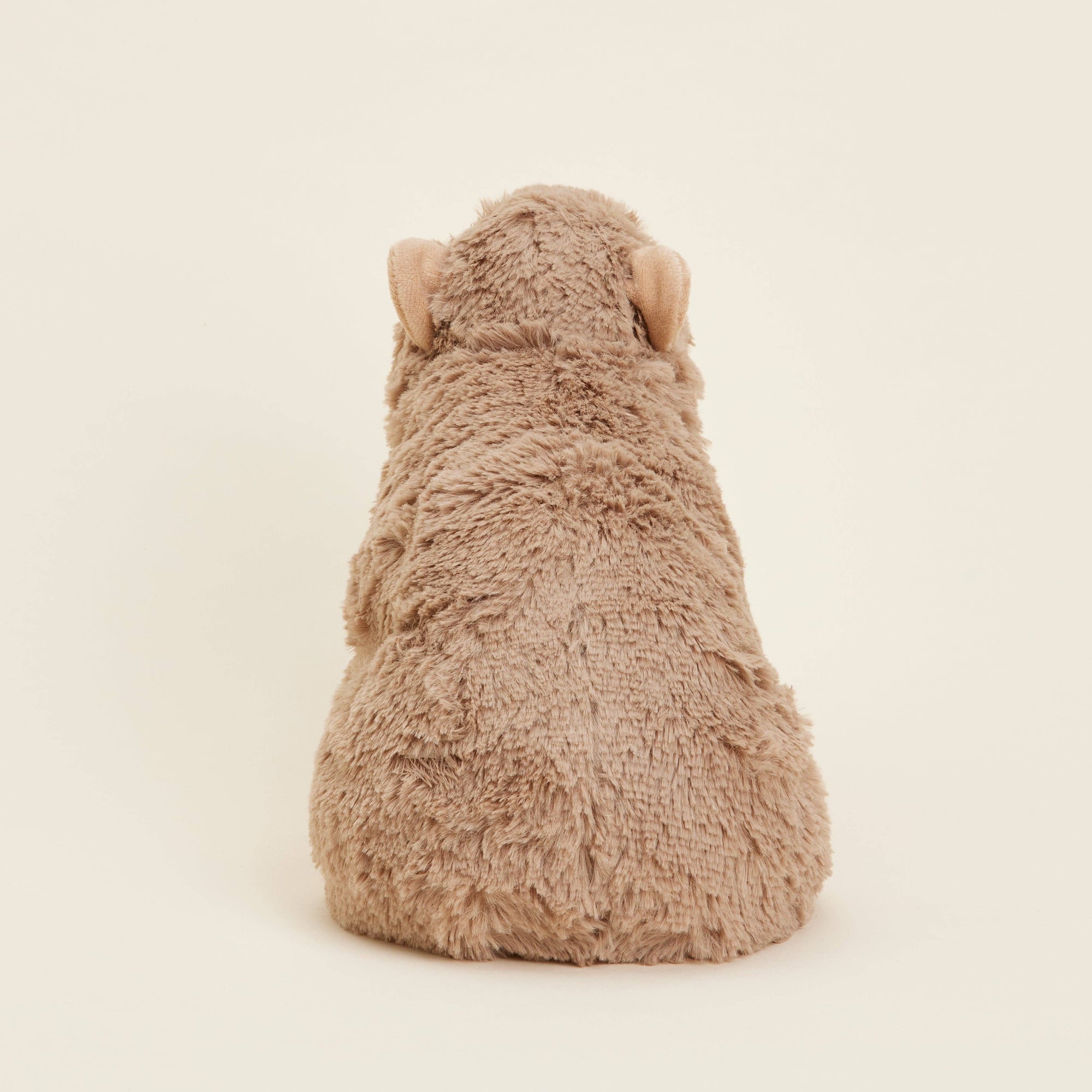 Plush toy resembling a capybara from behind on a beige background