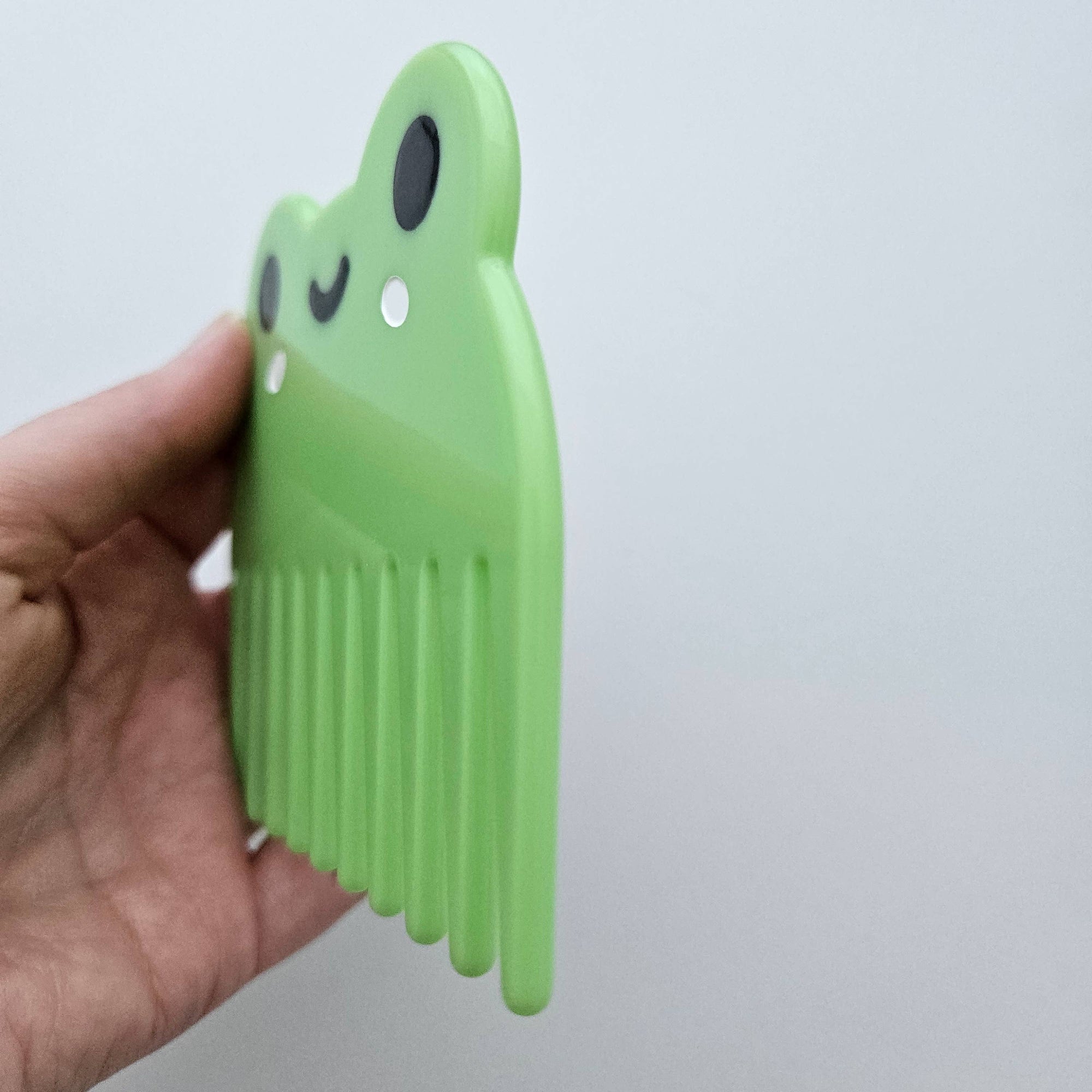 Green plastic comb with cartoon face held by a hand against a light gray background