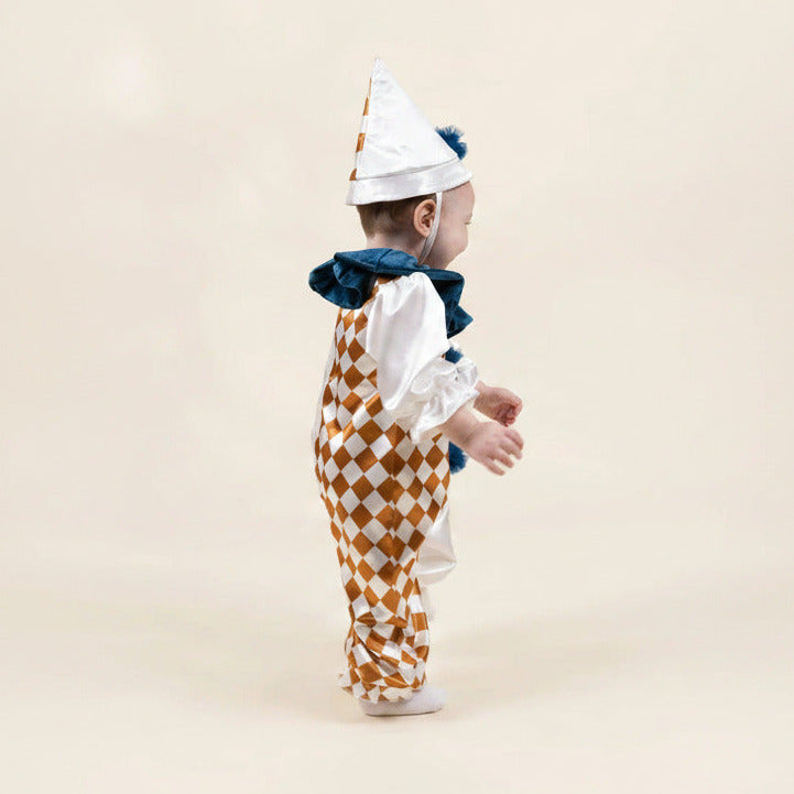A baby wearing a jester costume, shown from the back. The costume features a white and gold harlequin patterned jumpsuit with white ruffled sleeves, a dark blue ruffled collar, and a matching pointed white hat with gold and blue details.
