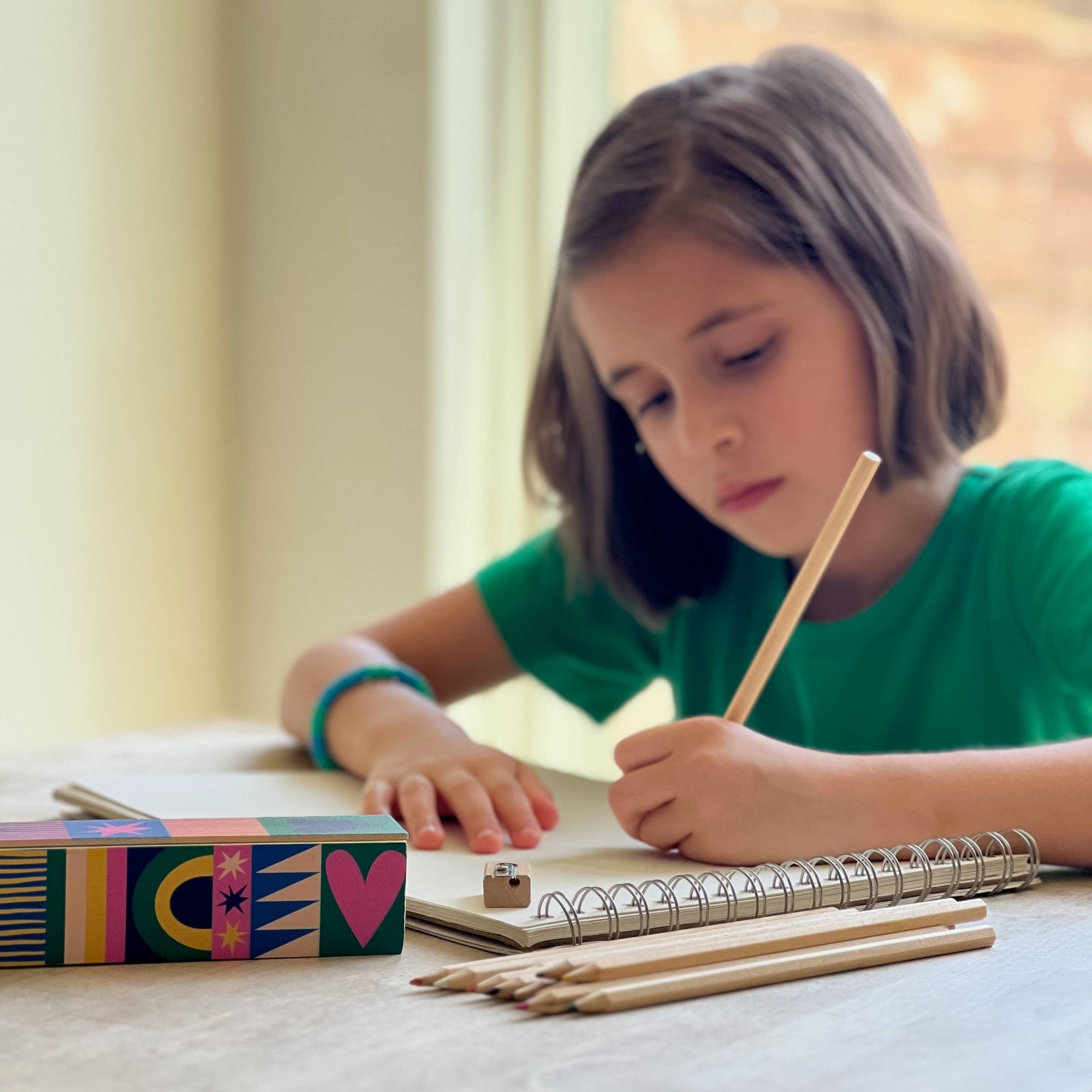 Young girl writing in a notebook with a pencil at a table.