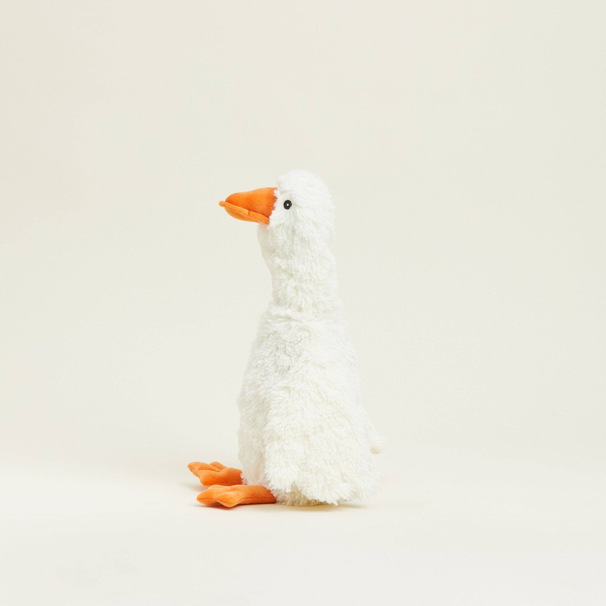 White plush duck toy with orange beak and feet on a beige background
