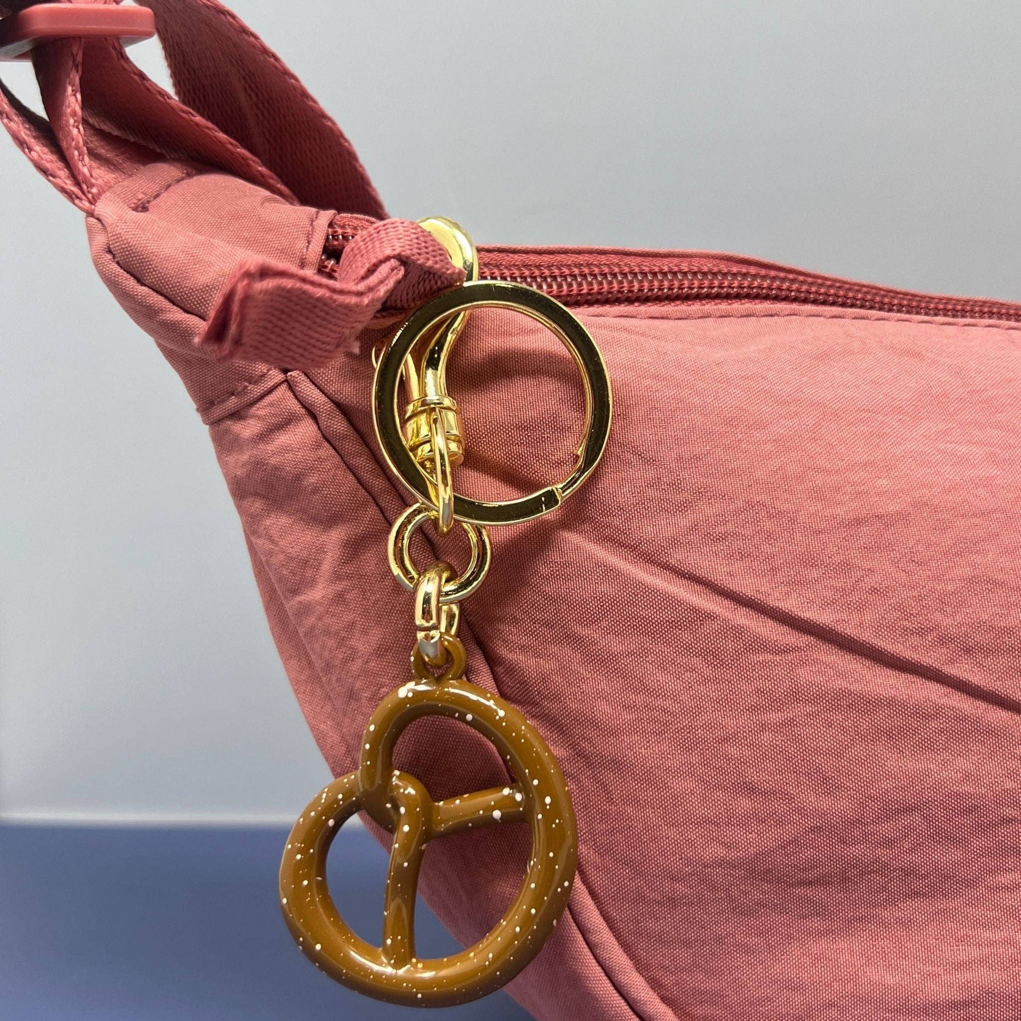 Gold pretzel-shaped keychain attached to a pink bag.