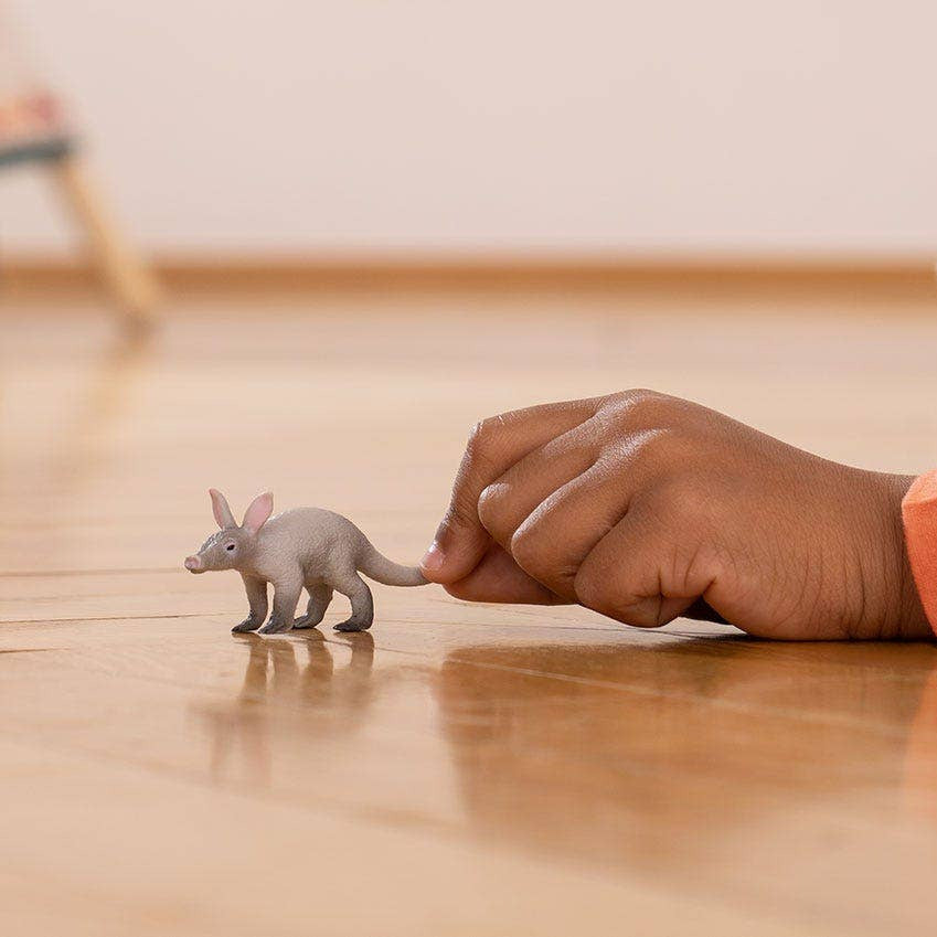 Hand interacting with a toy animal on a wooden floor