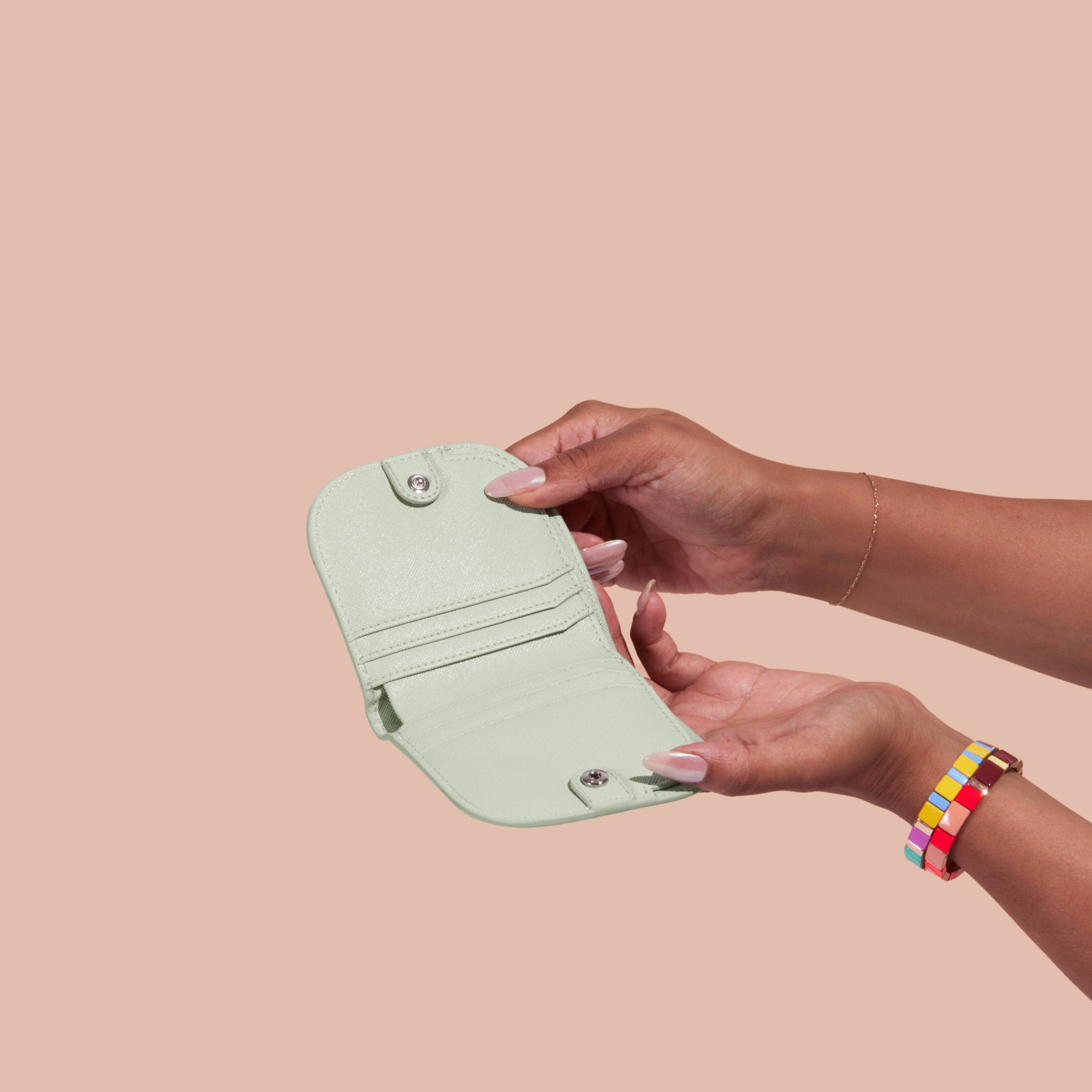 Person holding a light green wallet against a beige background