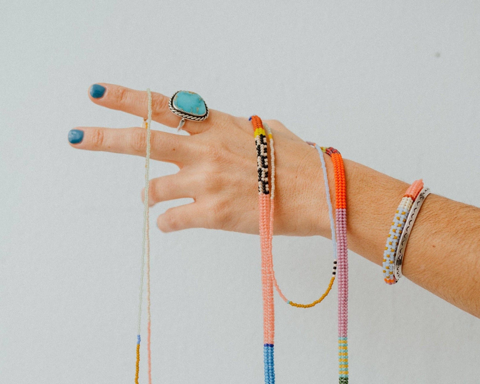 Hand wearing colorful bracelets and a ring on a light gray background