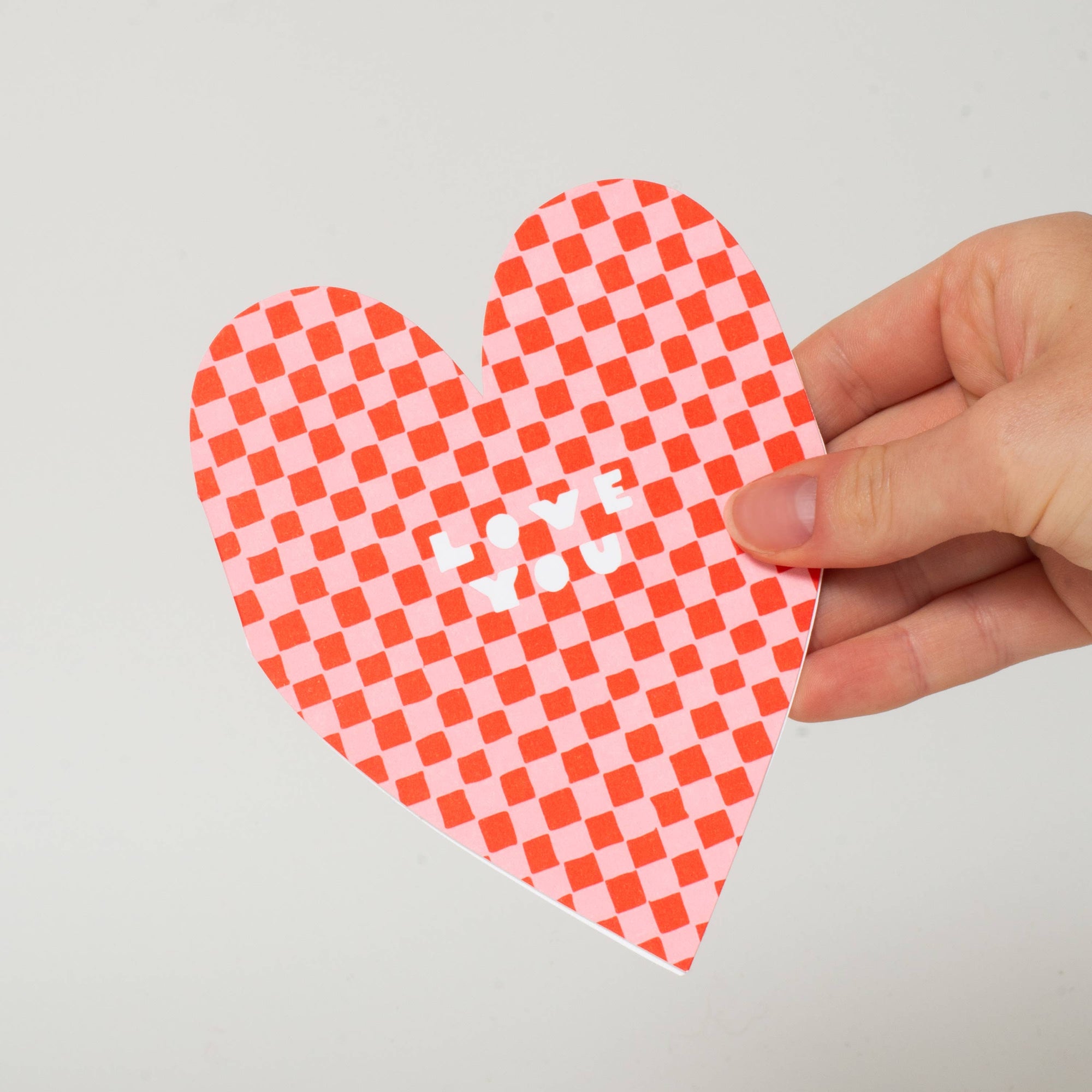 Hand holding a red and white checkered heart-shaped object on a light gray background