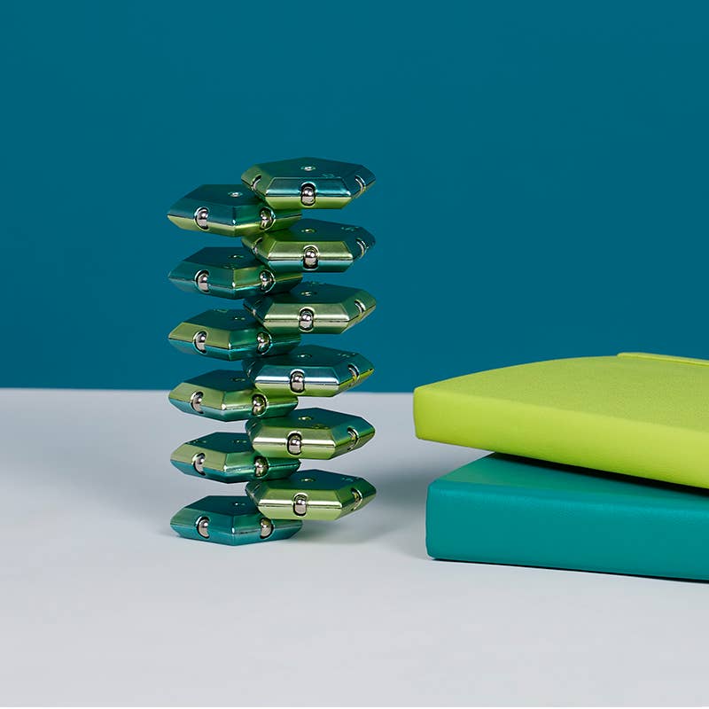 Green metallic sculpture on a white surface with a teal background