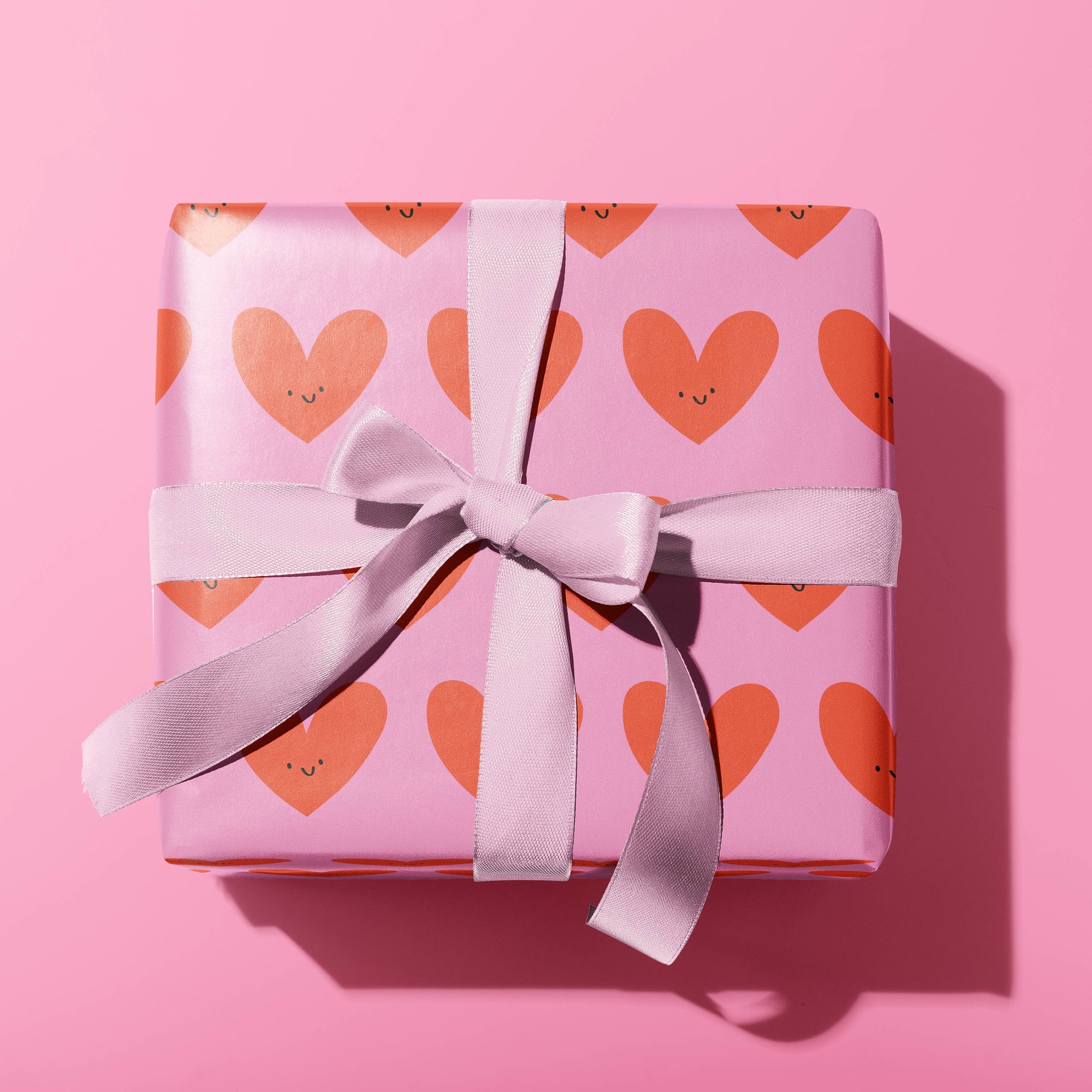 Gift box with heart pattern and pink ribbon on a pink background