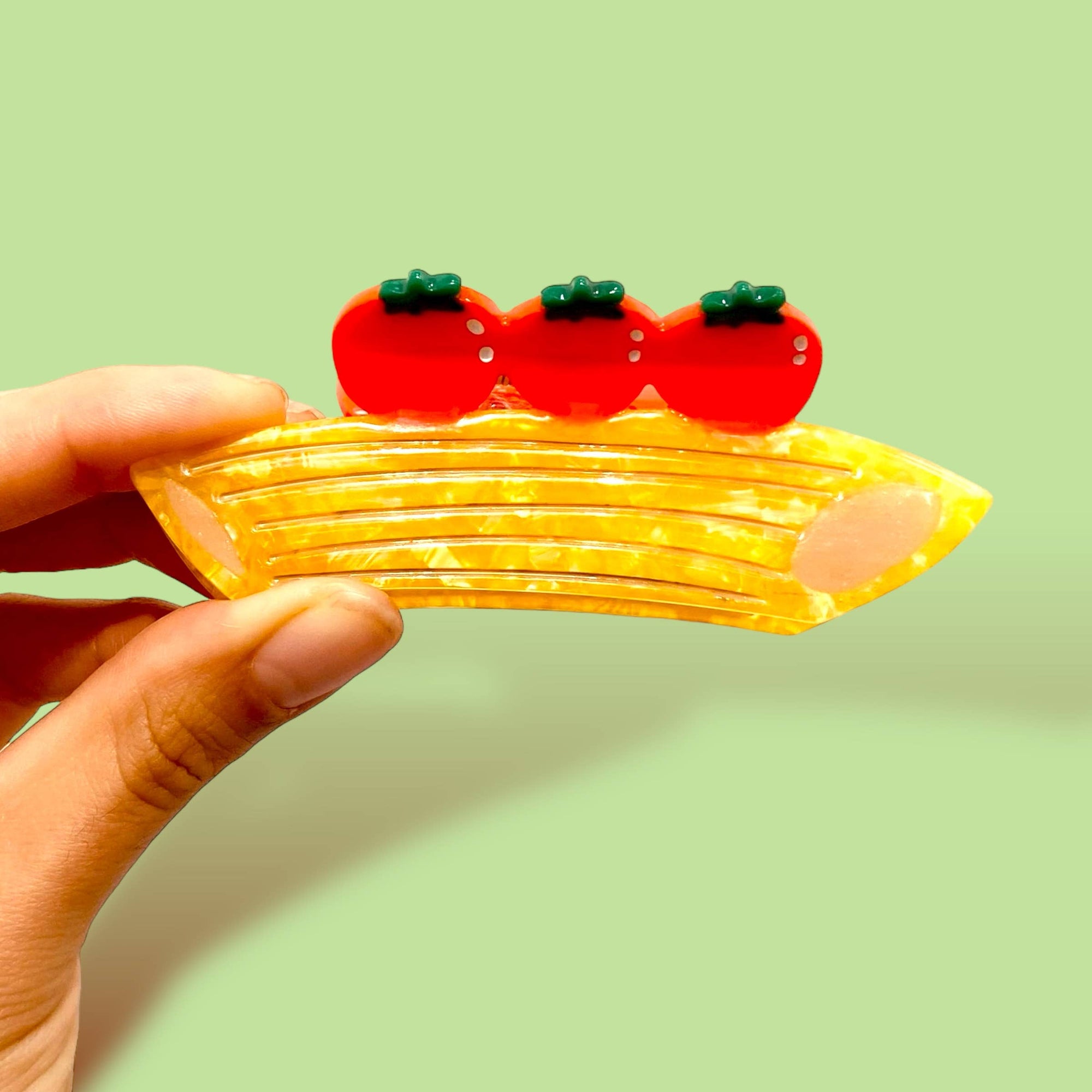 Hand holding a yellow pasta-shaped clip with red cherry tomatoes on a light green background