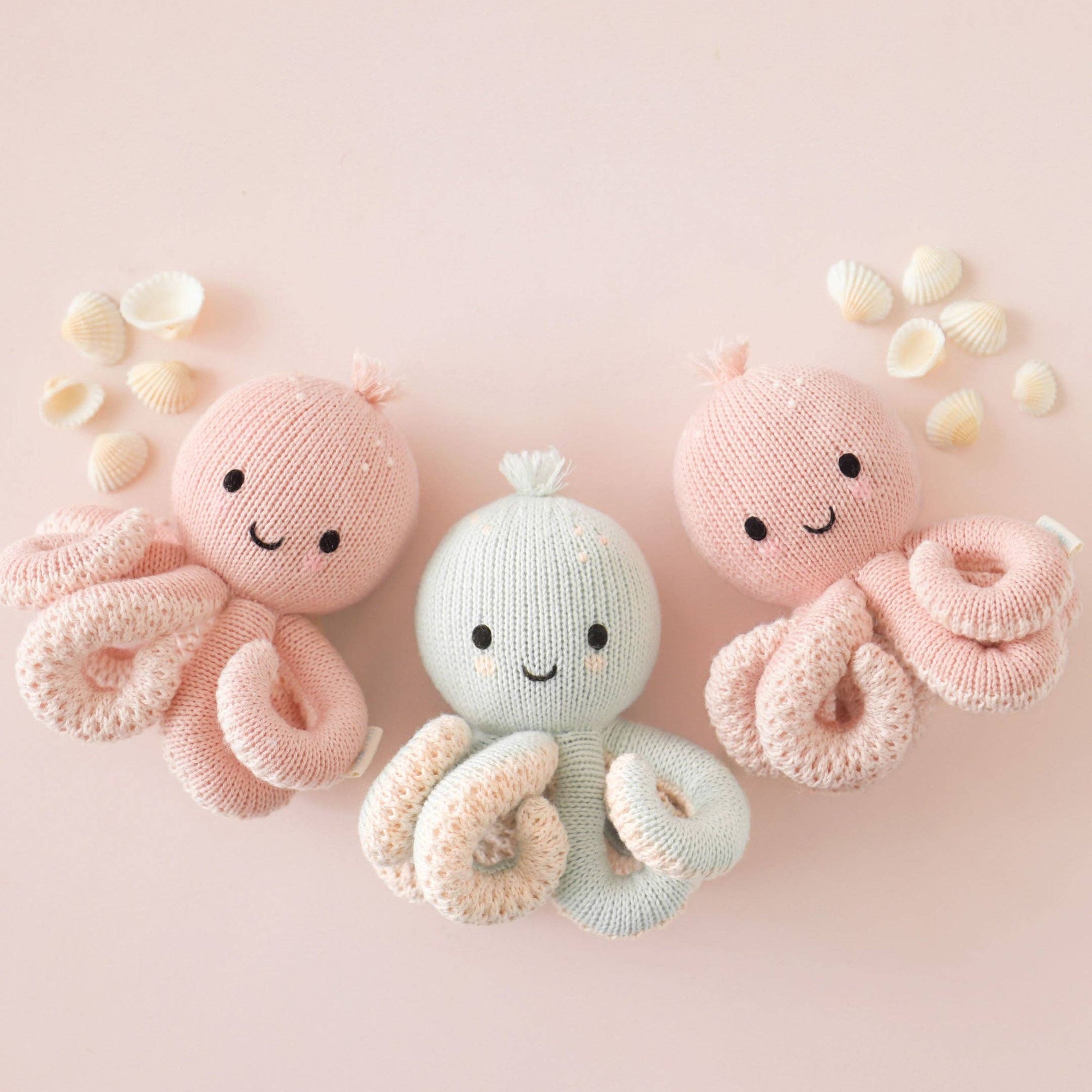 Two pink and one light blue knitted octopus toys on a pink background with small white flowers.
