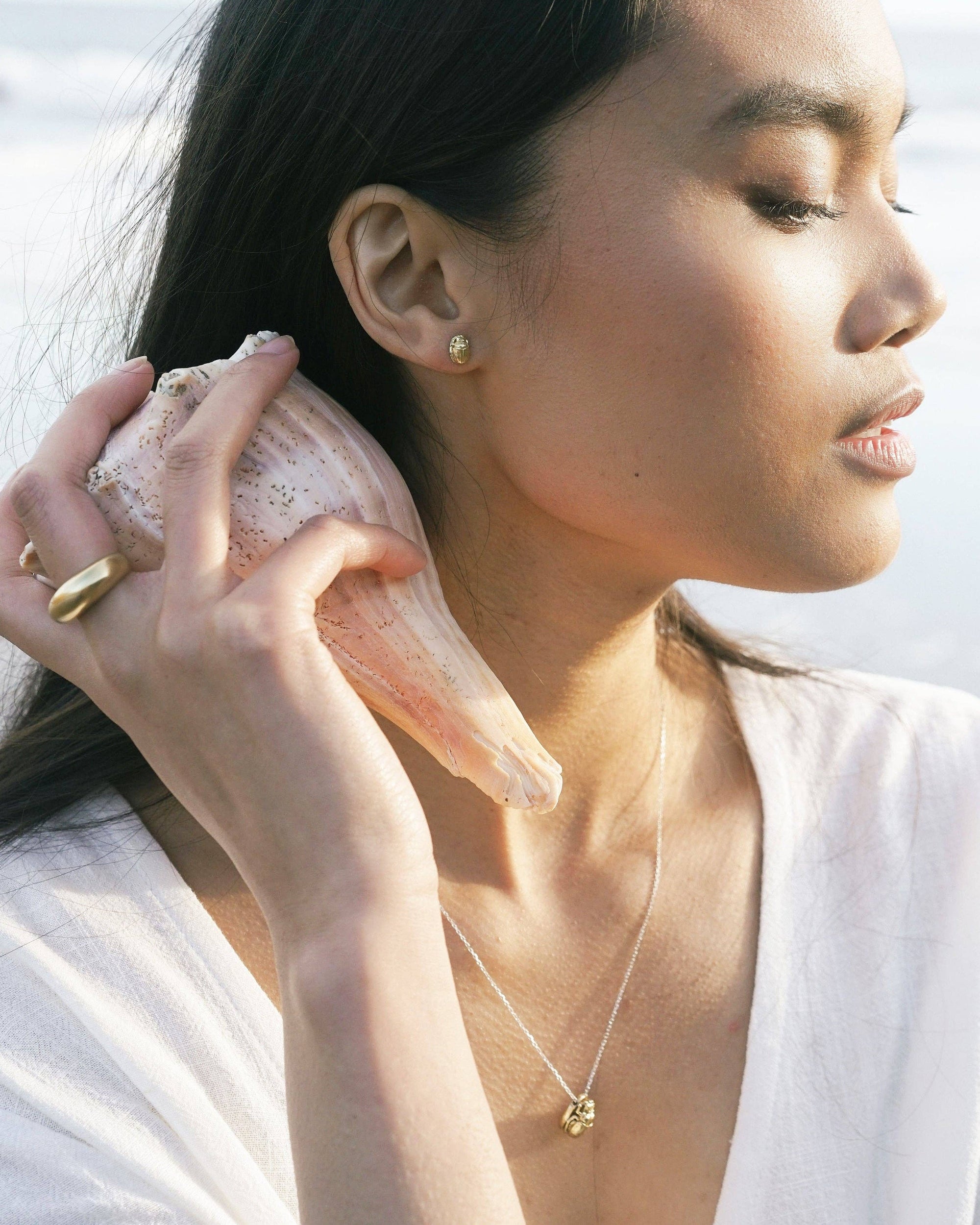 Woman holding a seashell to her ear with a blurred natural background