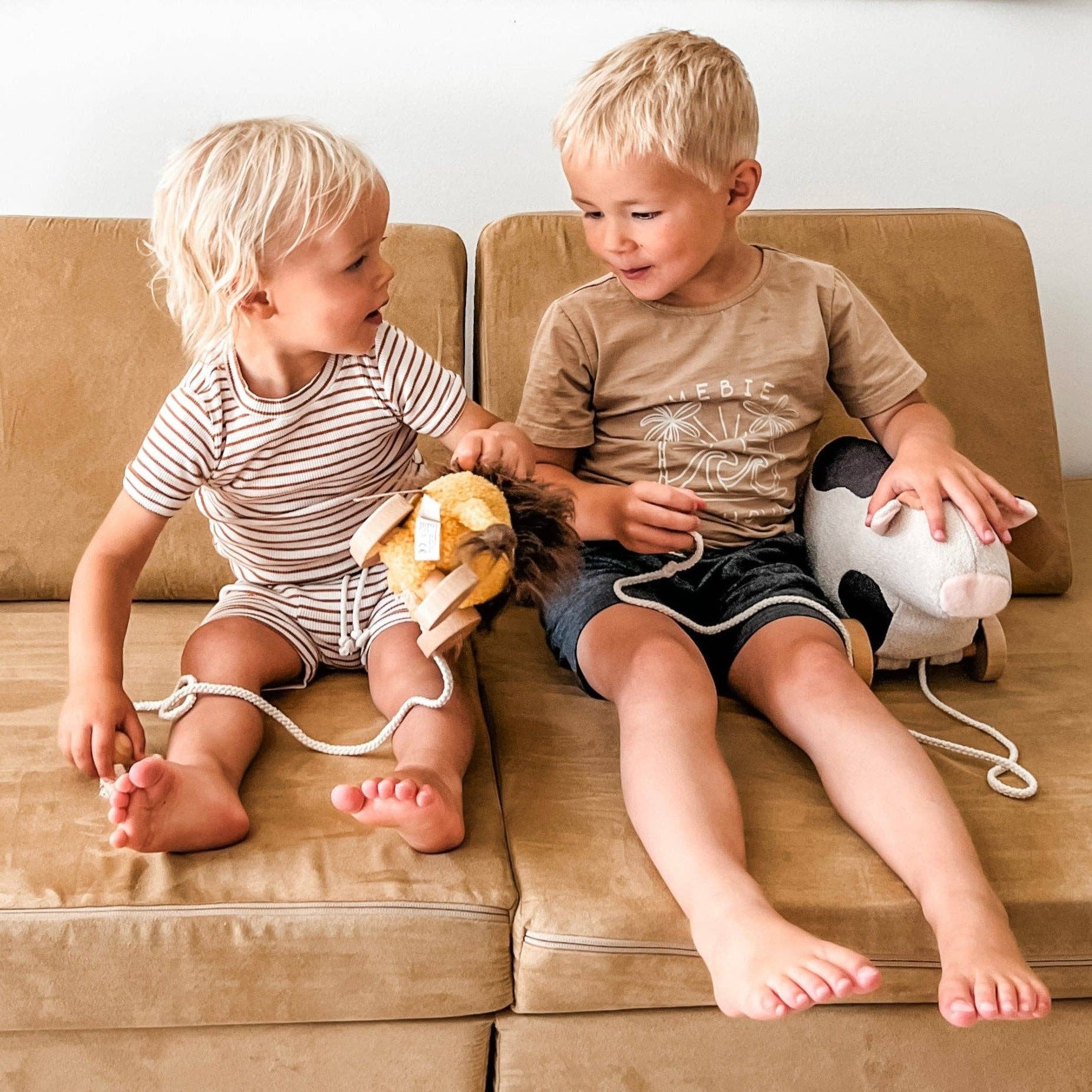 Two young children sitting on a couch with toys, engaged in play.