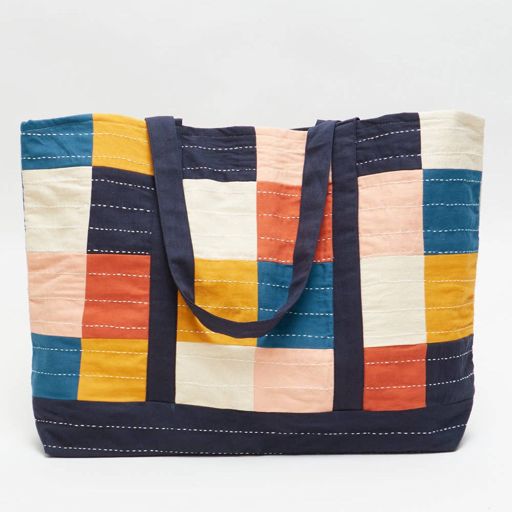 Colorful quilted tote bag with navy handles on a white background