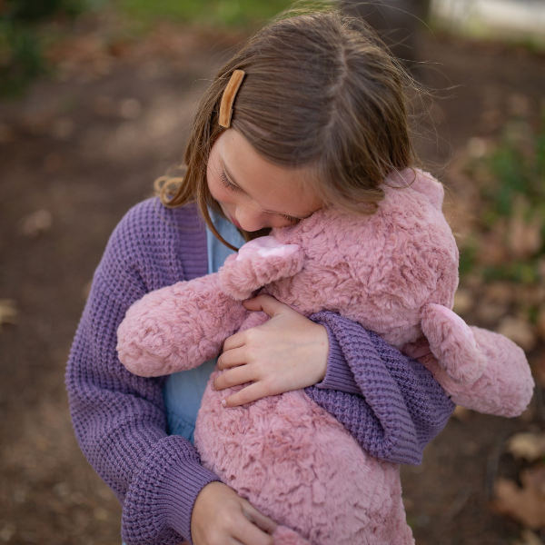 Child holding a pink teddy bear outdoors
