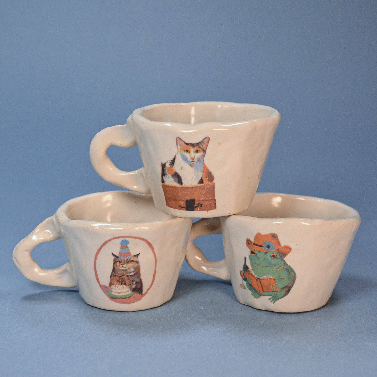 Three ceramic mugs with animal illustrations on a blue background