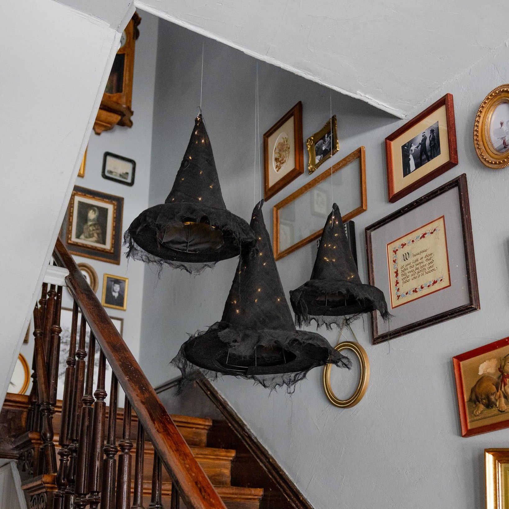 Decorative black witch hats hanging from the ceiling in a staircase with framed pictures on the wall.