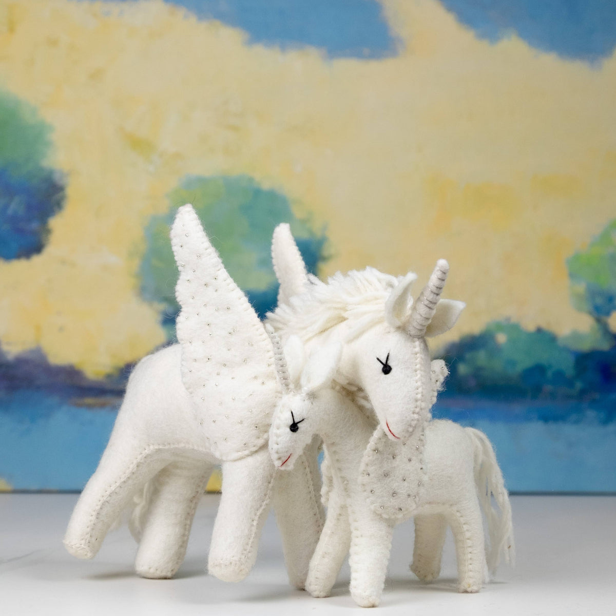 Two white unicorn toys with wings against a colorful abstract background
